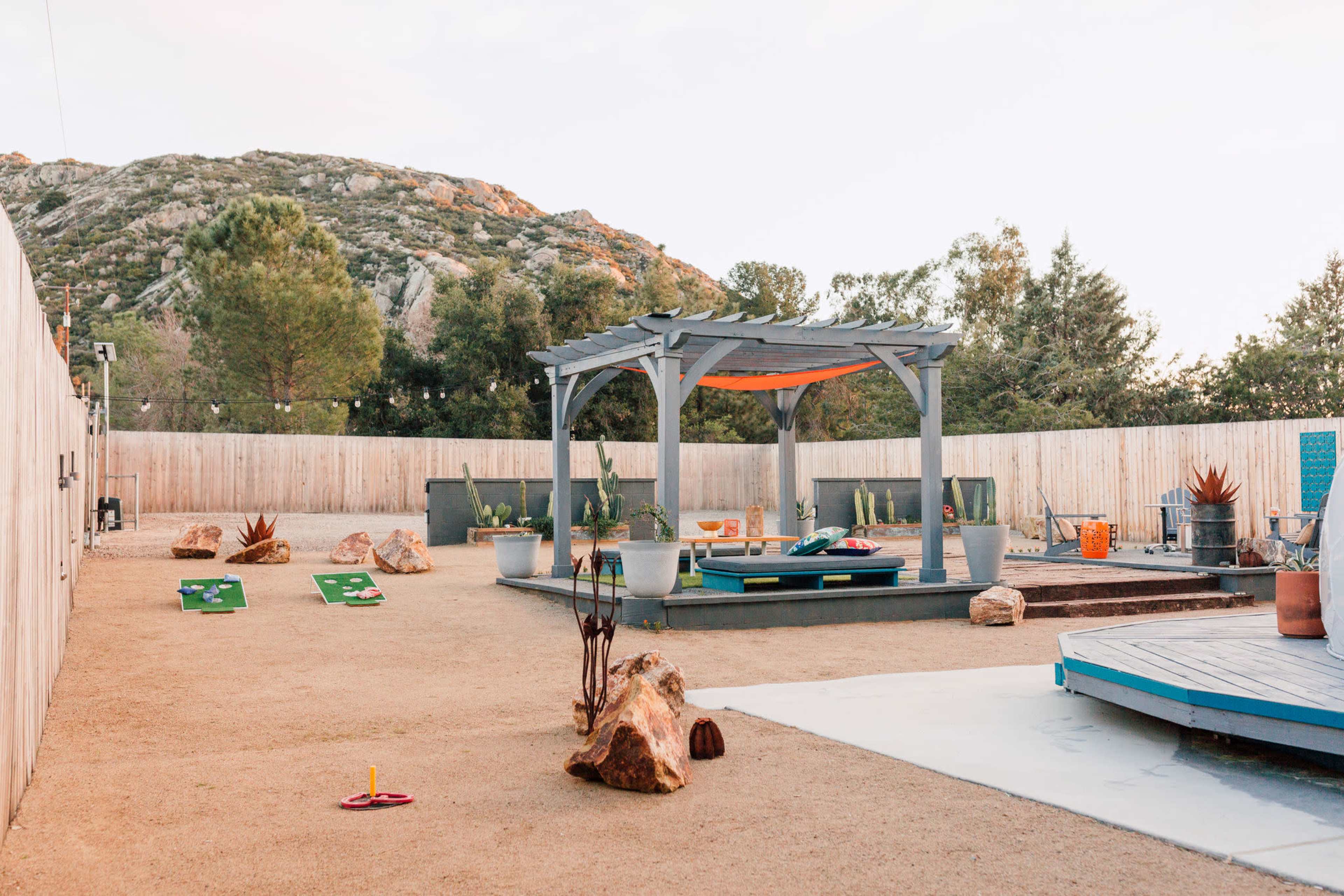 An outdoor recreational area with a pergola, lawn games, and a landscaped environment amidst rocky hills.