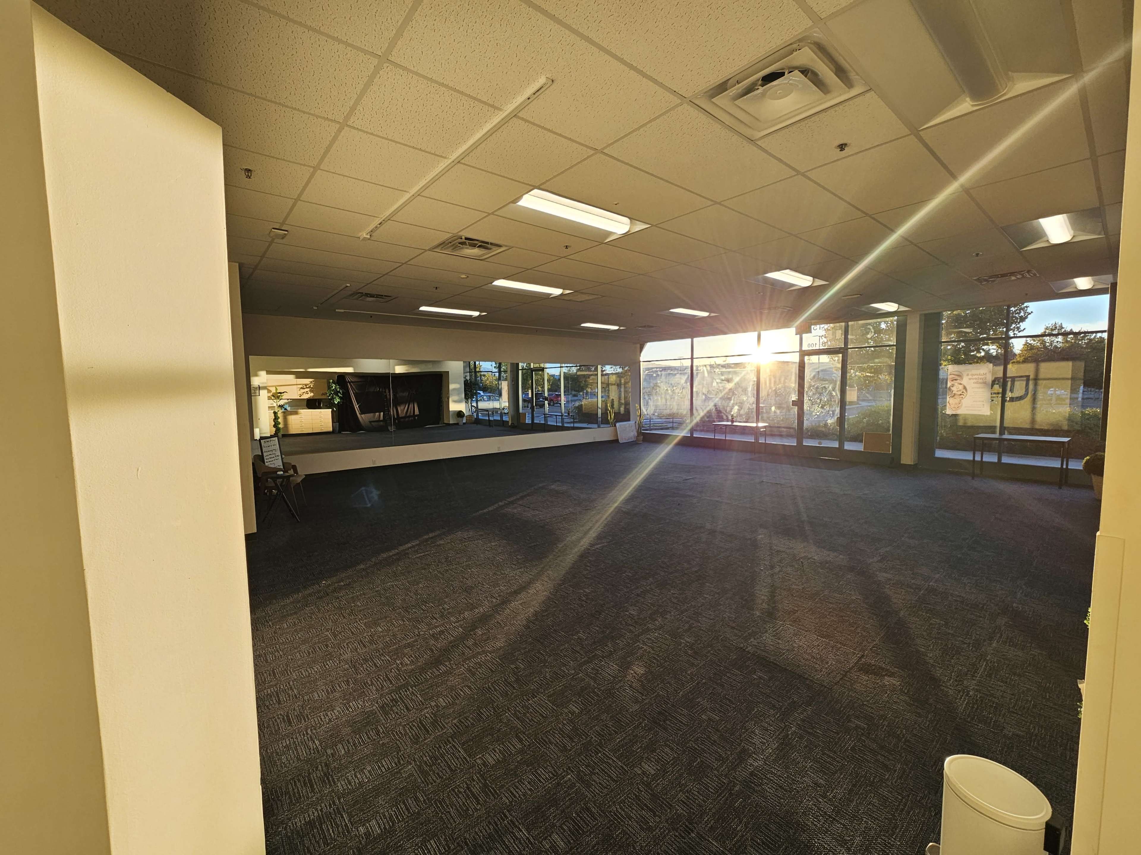 The image shows an empty office space with large windows allowing sunlight to stream in, casting rays across the floor.
