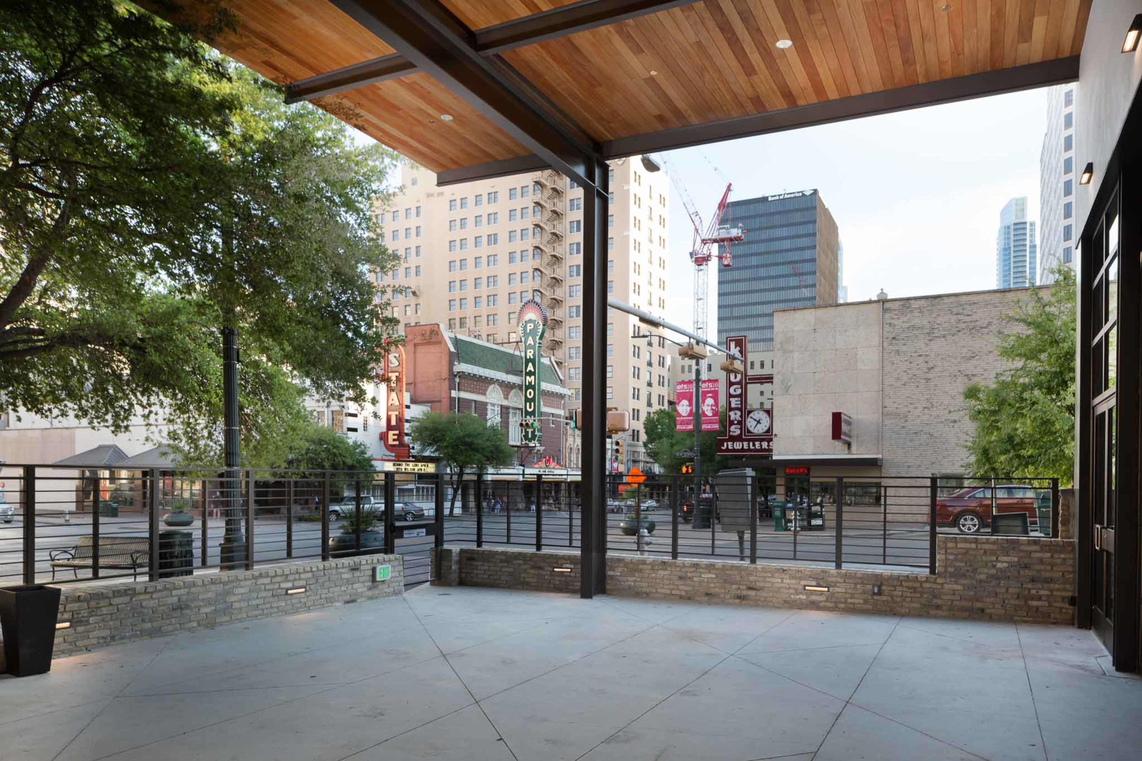 A spacious outdoor area of a building overlooking a city street with visible commercial signs and greenery.