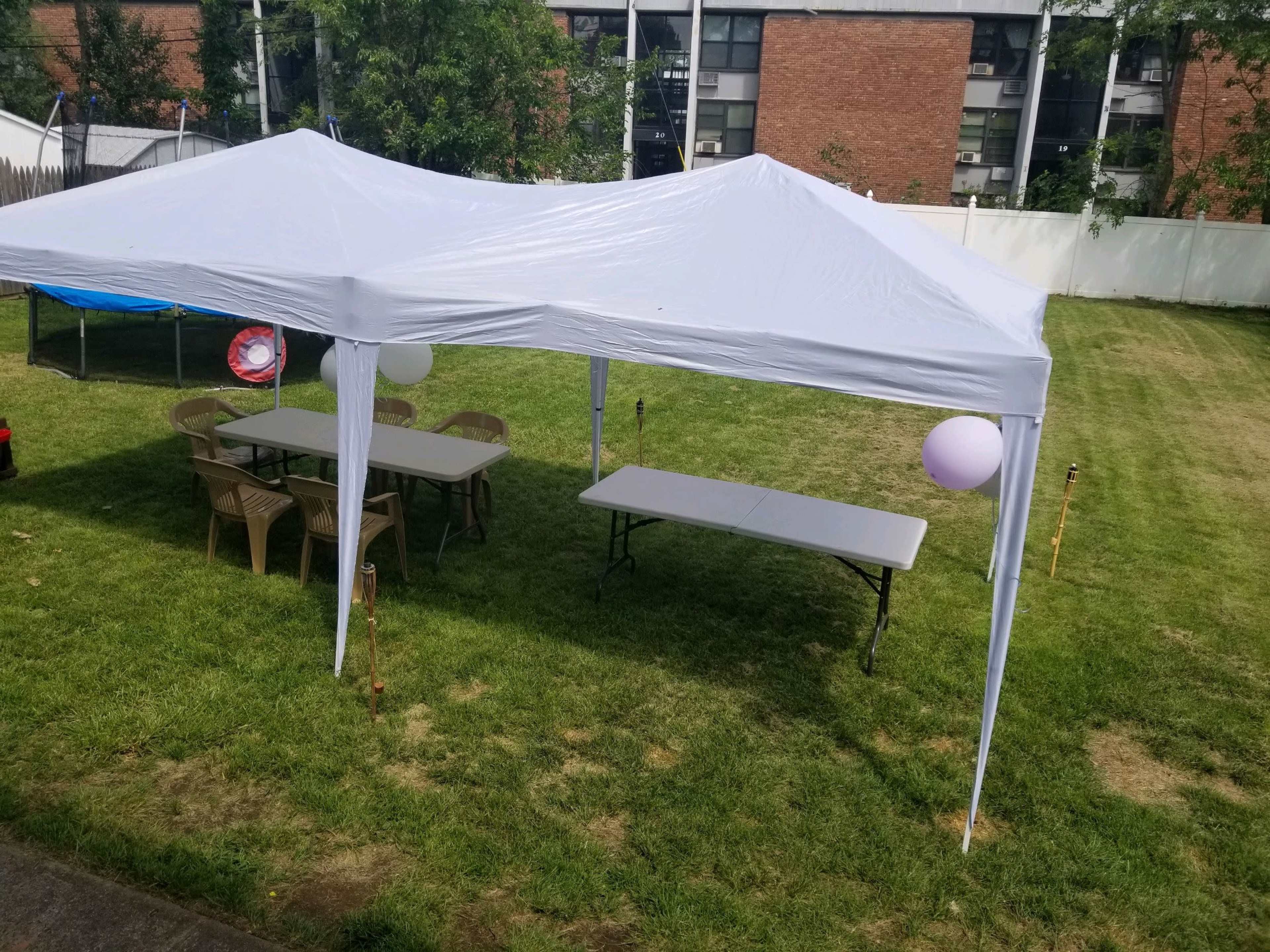 A white canopy tent is set up on a grassy area with folding tables and chairs underneath.