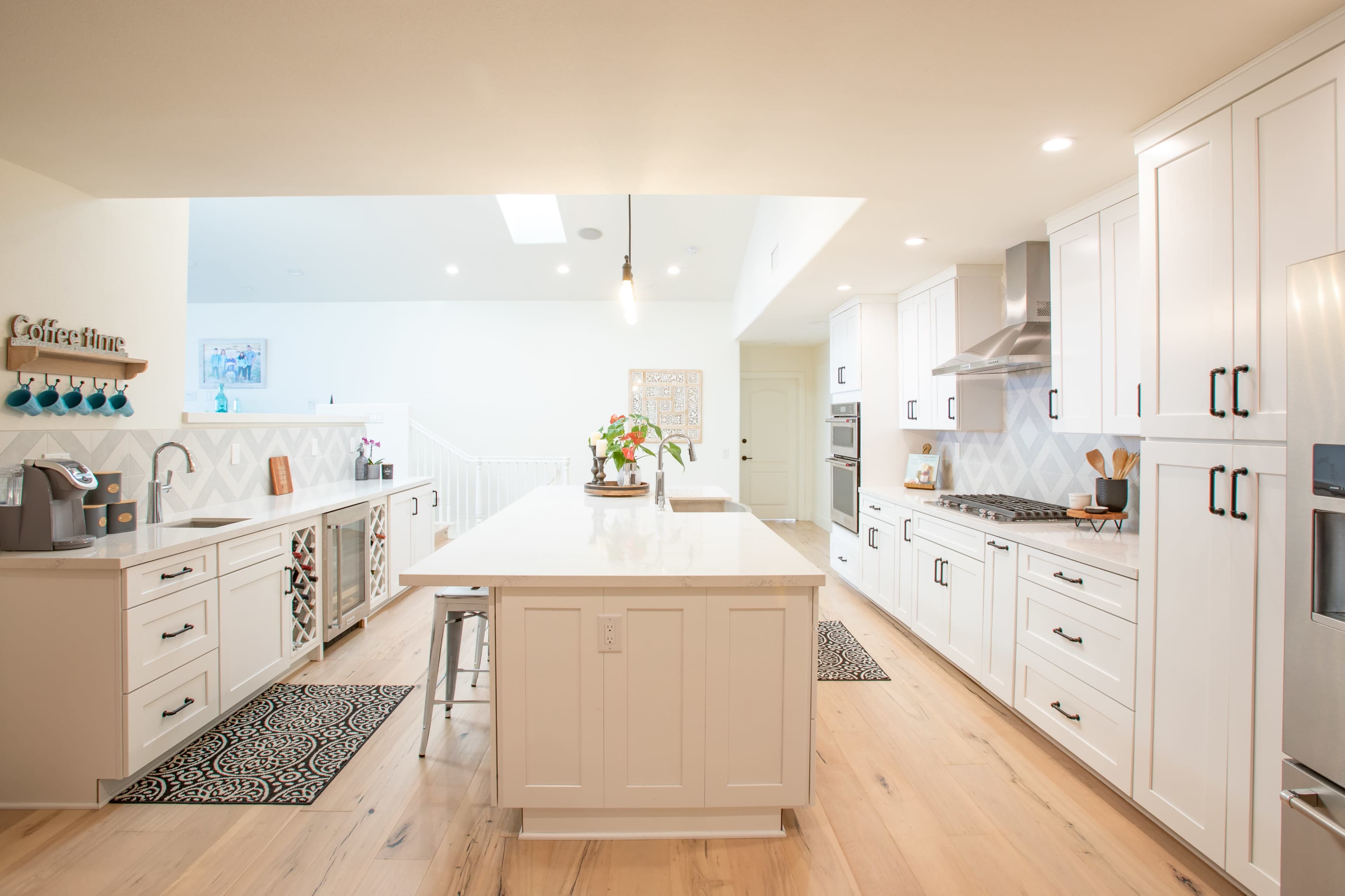 A modern kitchen features white cabinetry, a central island with a light countertop, and stainless steel appliances.