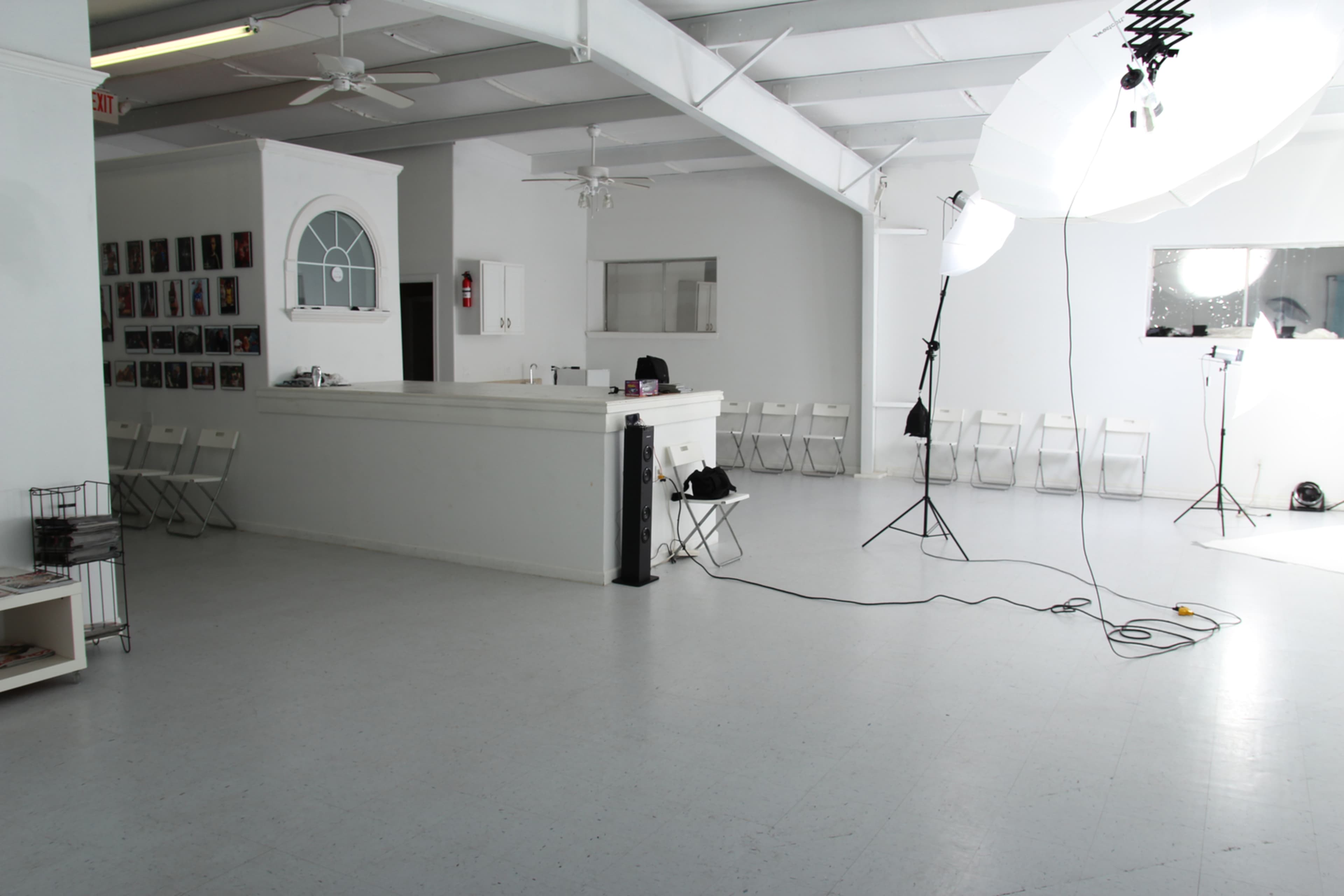 A spacious, well-lit studio with a white interior featuring a reception area, rows of white chairs, and photography equipment set up in one corner.
