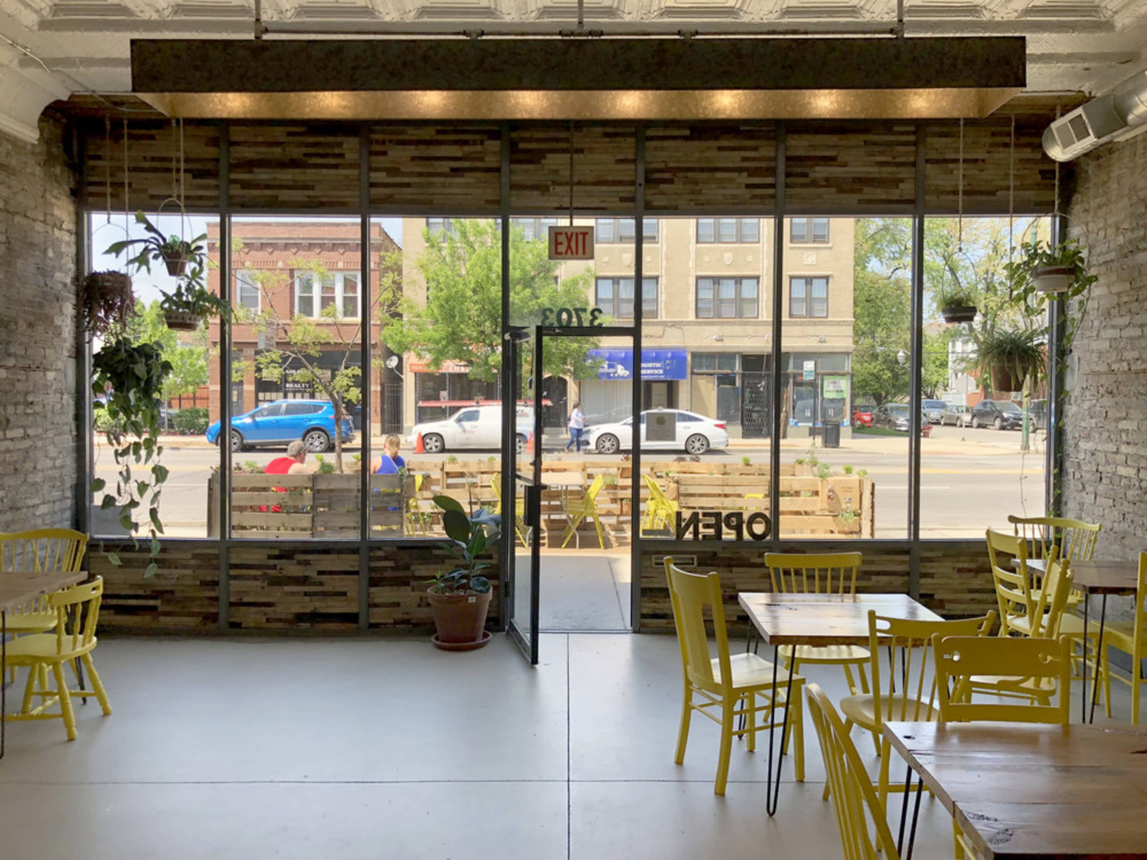 A brightly lit café with yellow chairs and large windows showcasing a street view.