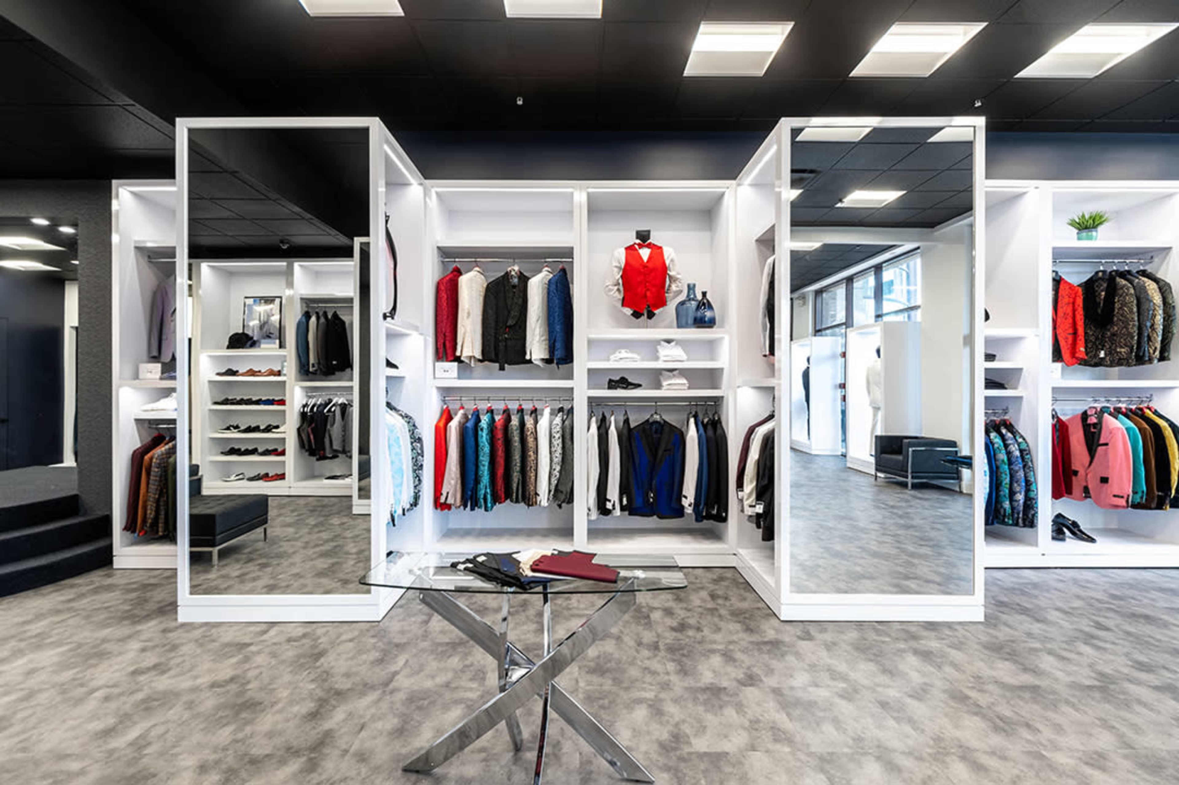 A modern clothing store interior with displays of neatly arranged garments, shoes, and mirrors in a bright, spacious environment.