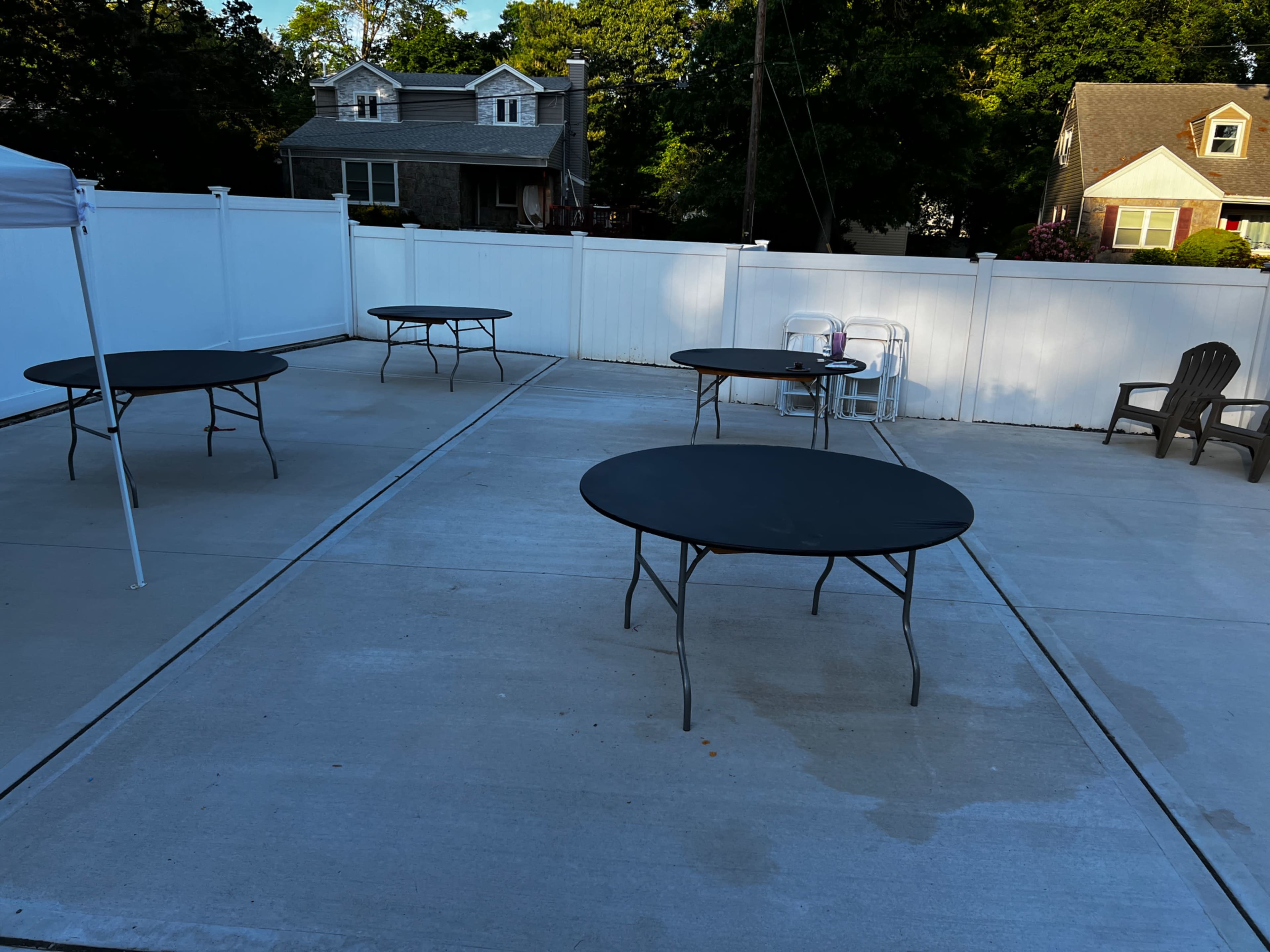 The image shows several black folding tables arranged in a paved outdoor area surrounded by a white fence.