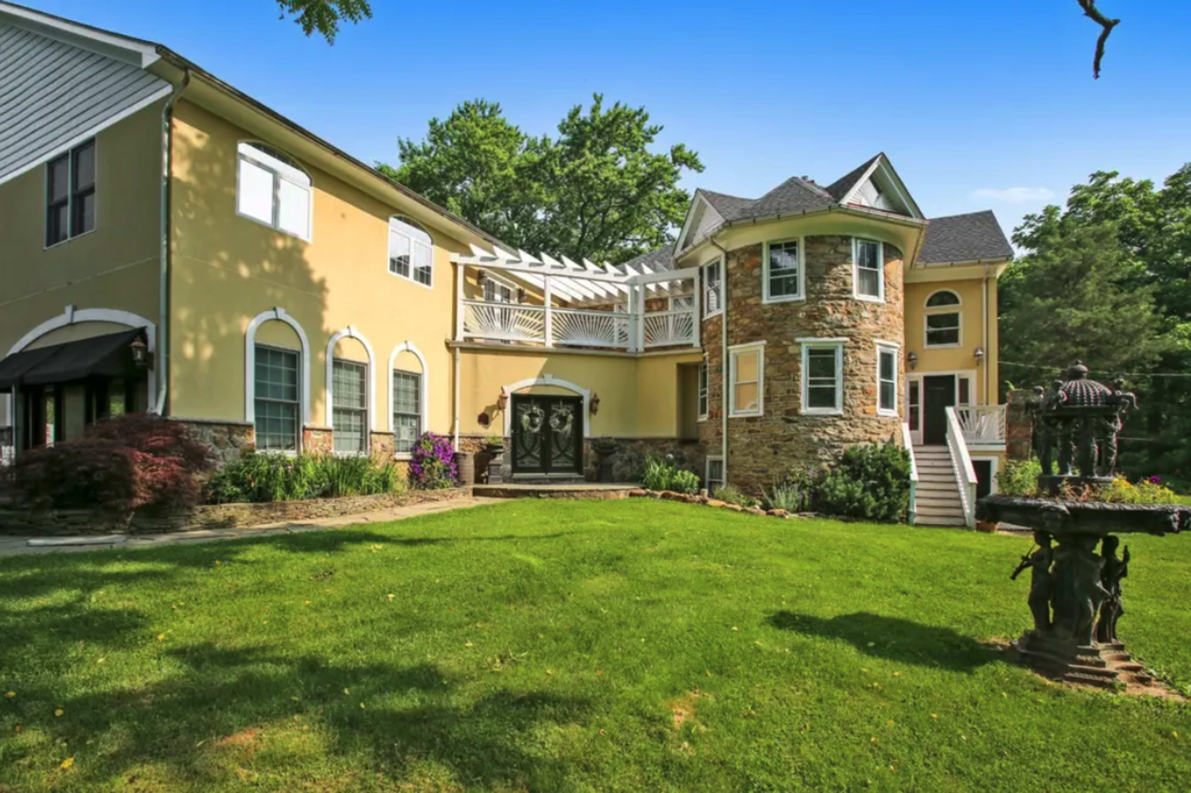 A large multi-story house with a stone and stucco exterior, surrounded by a well-maintained lawn and a decorative fountain in the foreground.