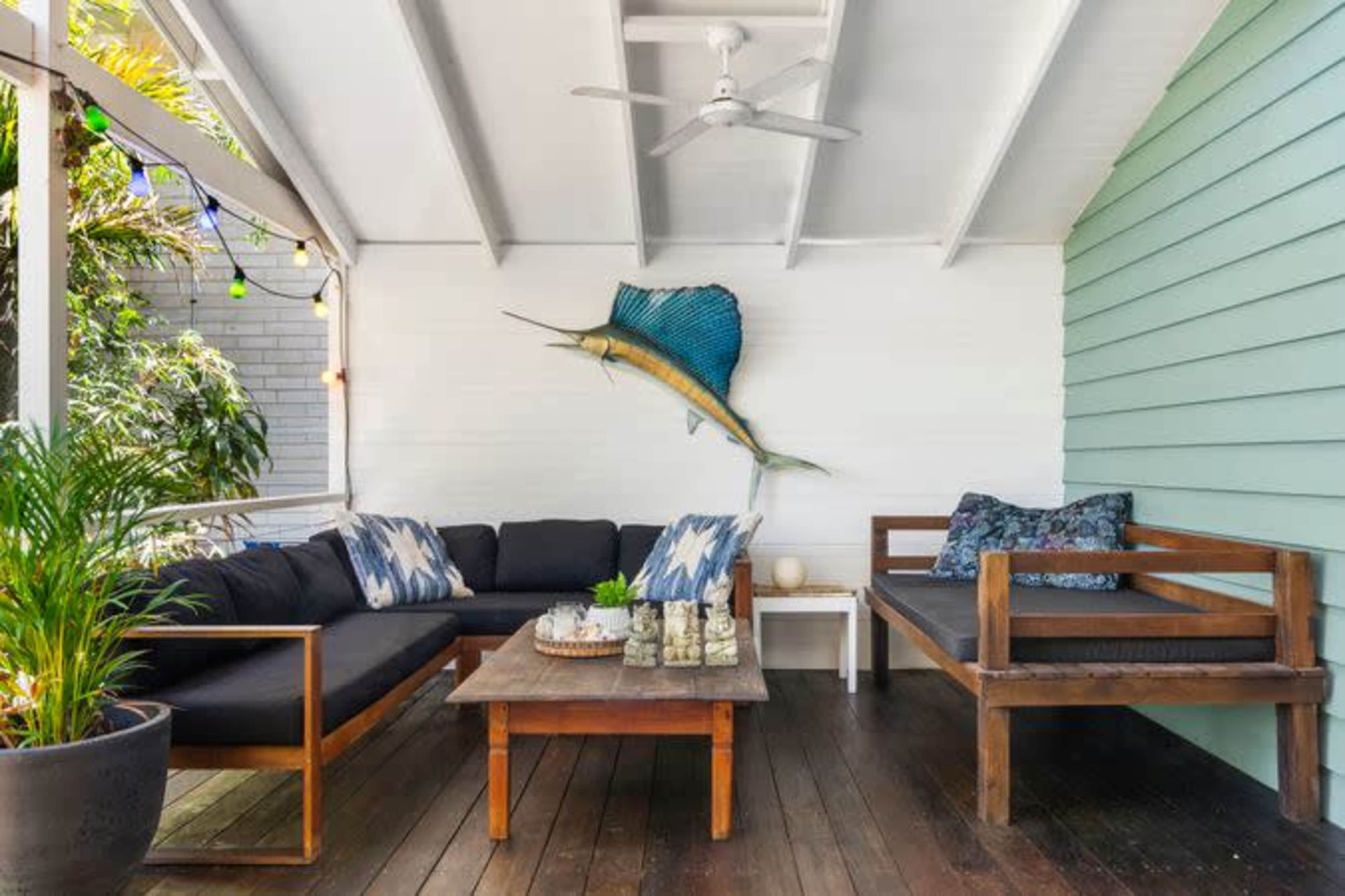 A covered porch with a dark sofa, a wooden coffee table, and a mounted fish decoration on the wall.