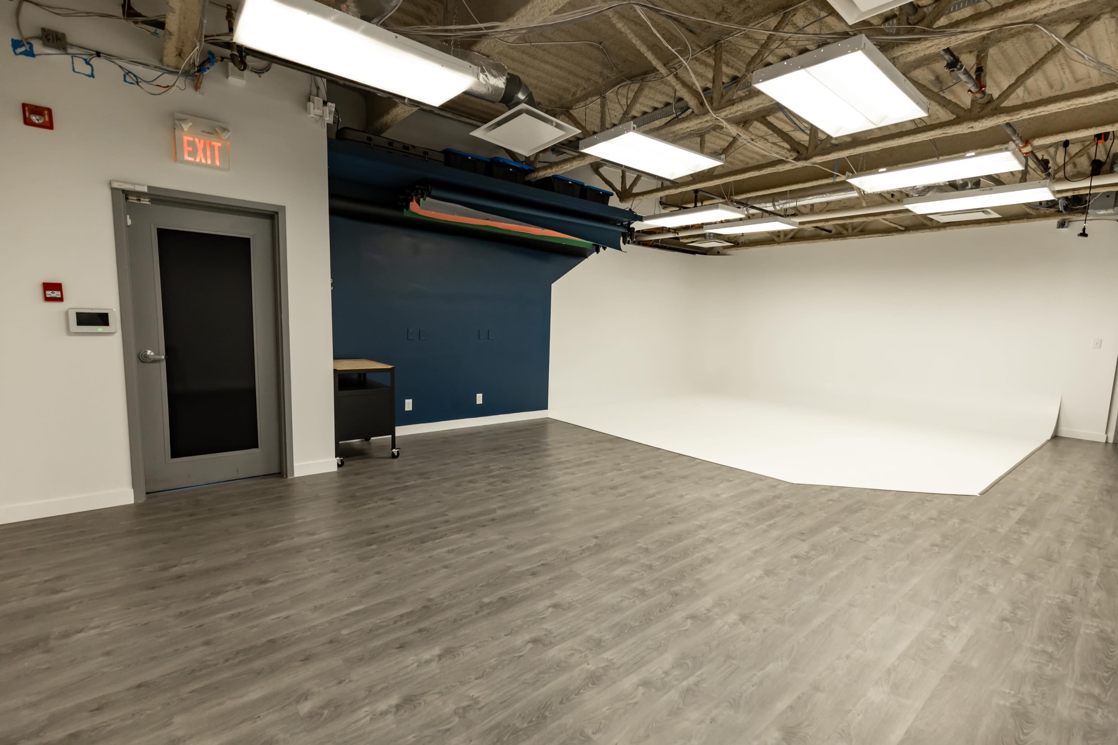 A studio space with a dark blue accented wall, a white backdrop area, and wooden flooring.