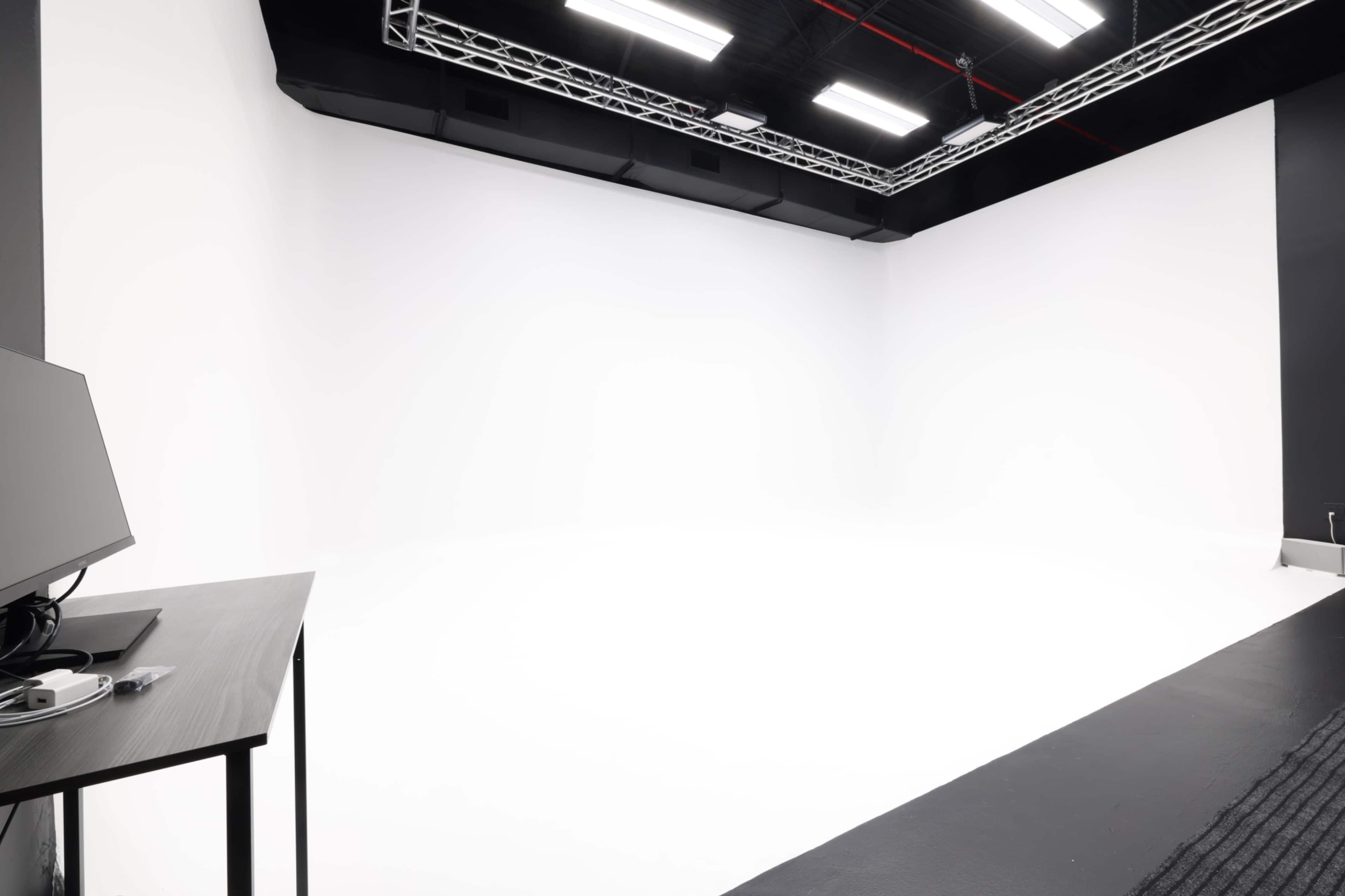 The image shows a spacious photography studio with a clean white backdrop and minimal furnishings.
