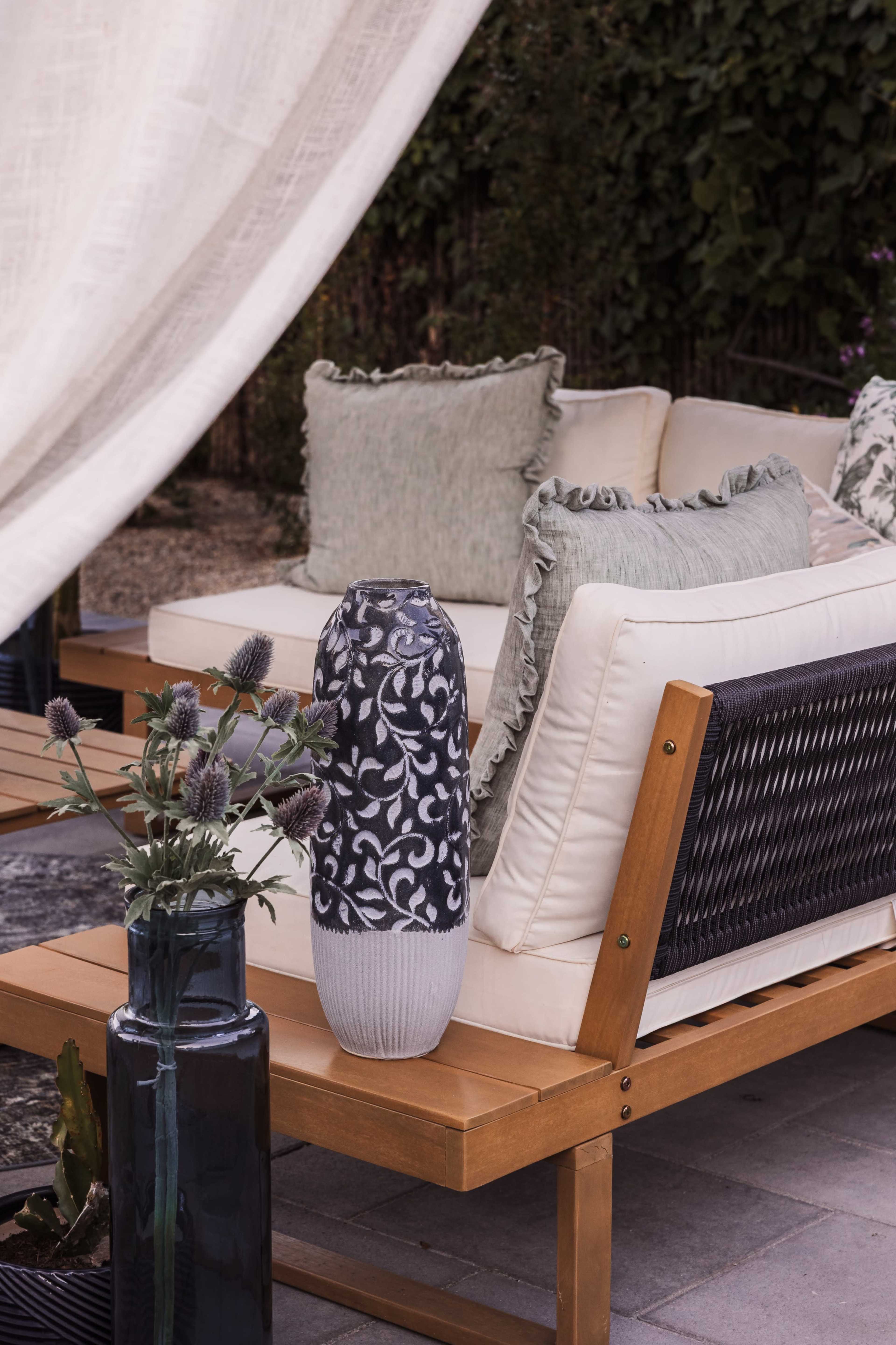 A decorative vase and a floral arrangement are placed on a wooden table next to a cozy outdoor seating area with cushions.