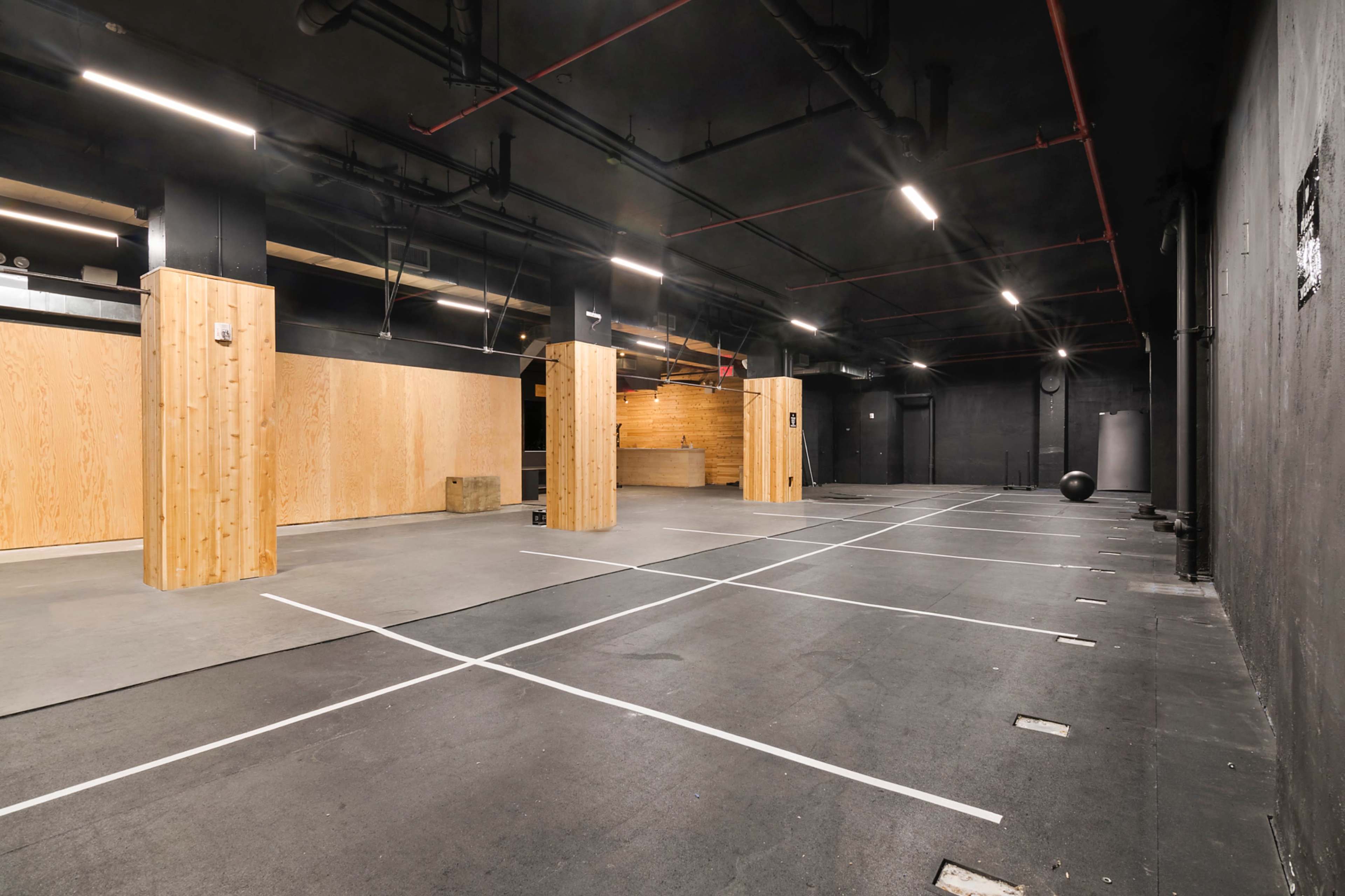 The image shows an empty gym space with black walls, wooden accents, and marked areas on the floor.