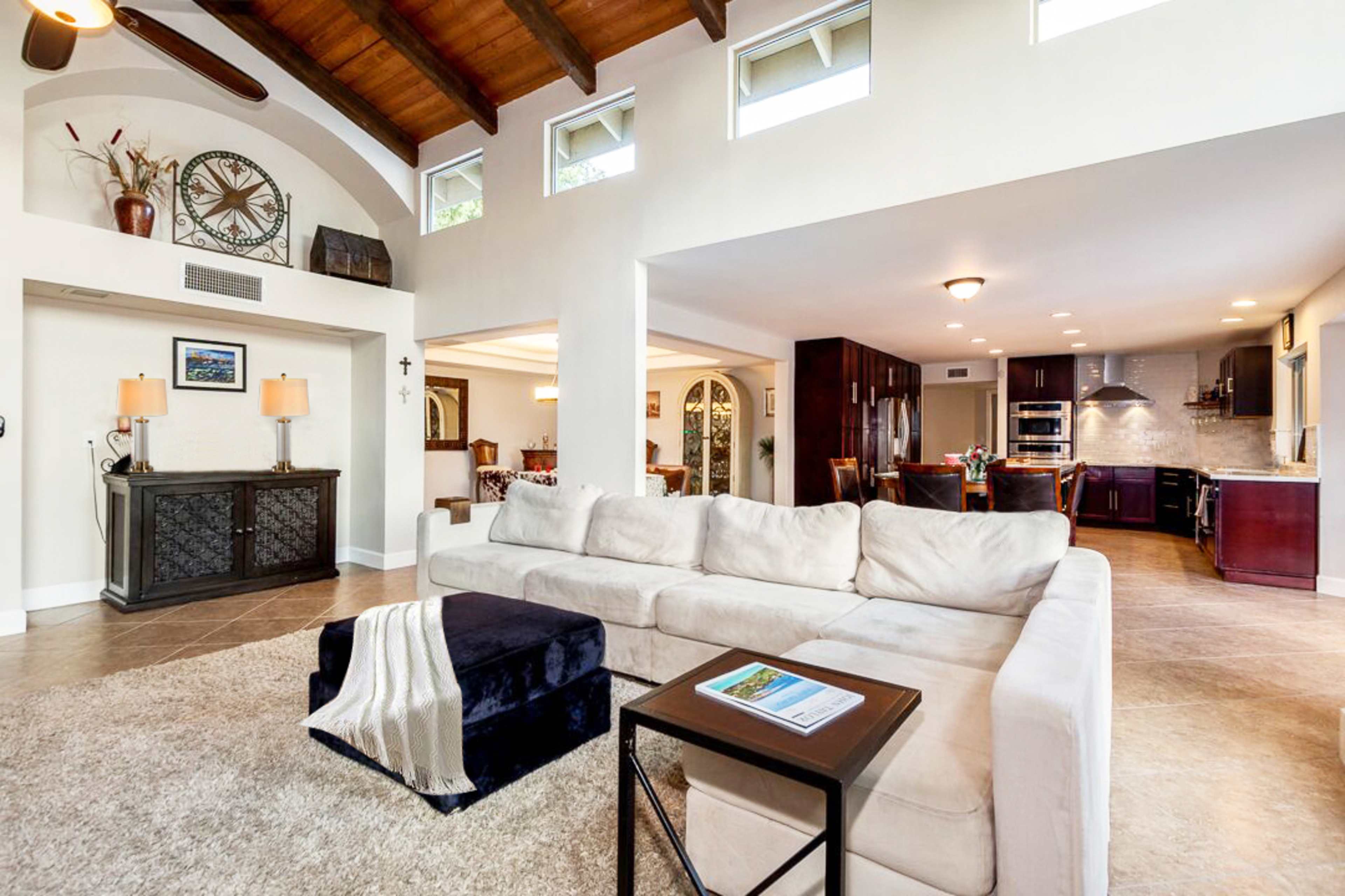 A spacious living room with a large sectional sofa, a coffee table, and an open layout leading to a dining area and kitchen.