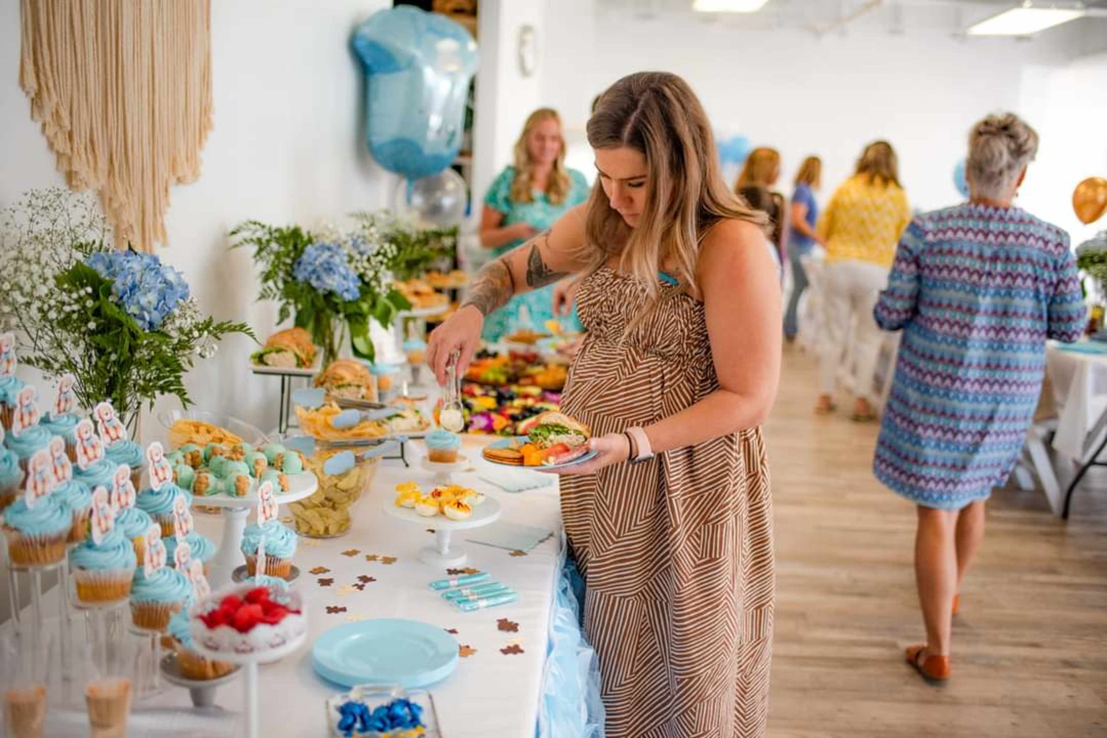 A woman in a patterned dress serves herself from a table filled with various desserts and snacks during a celebration.