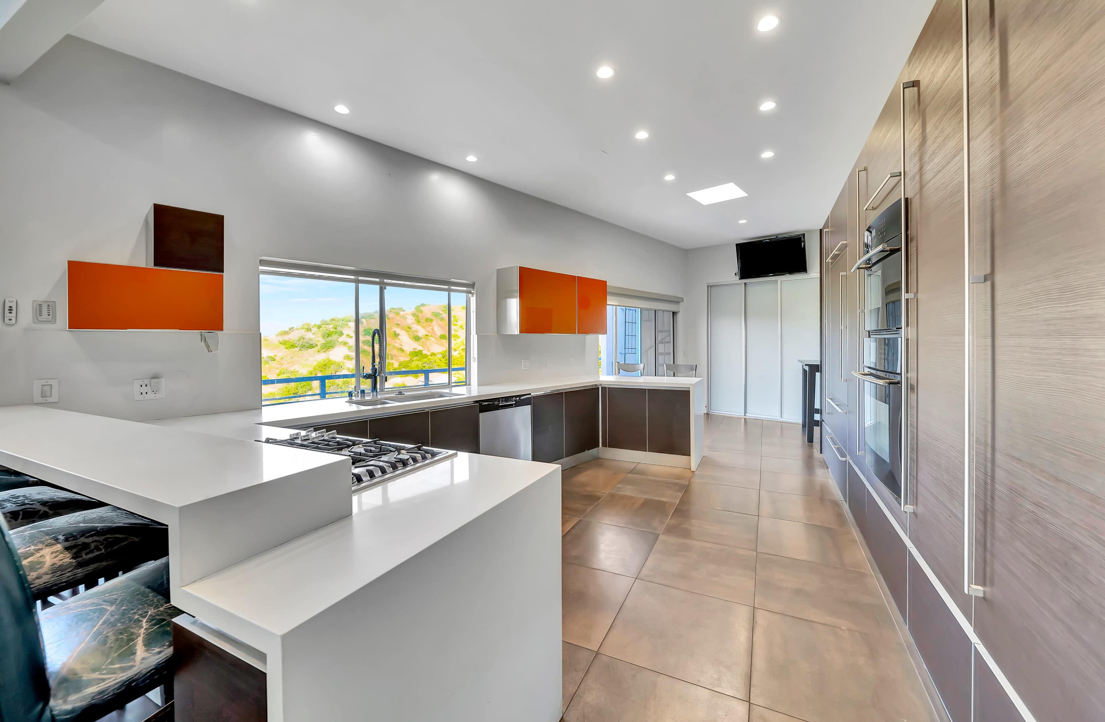 A modern kitchen features sleek cabinetry, a large island with a gas stove, and windows that offer a view of the outdoors.