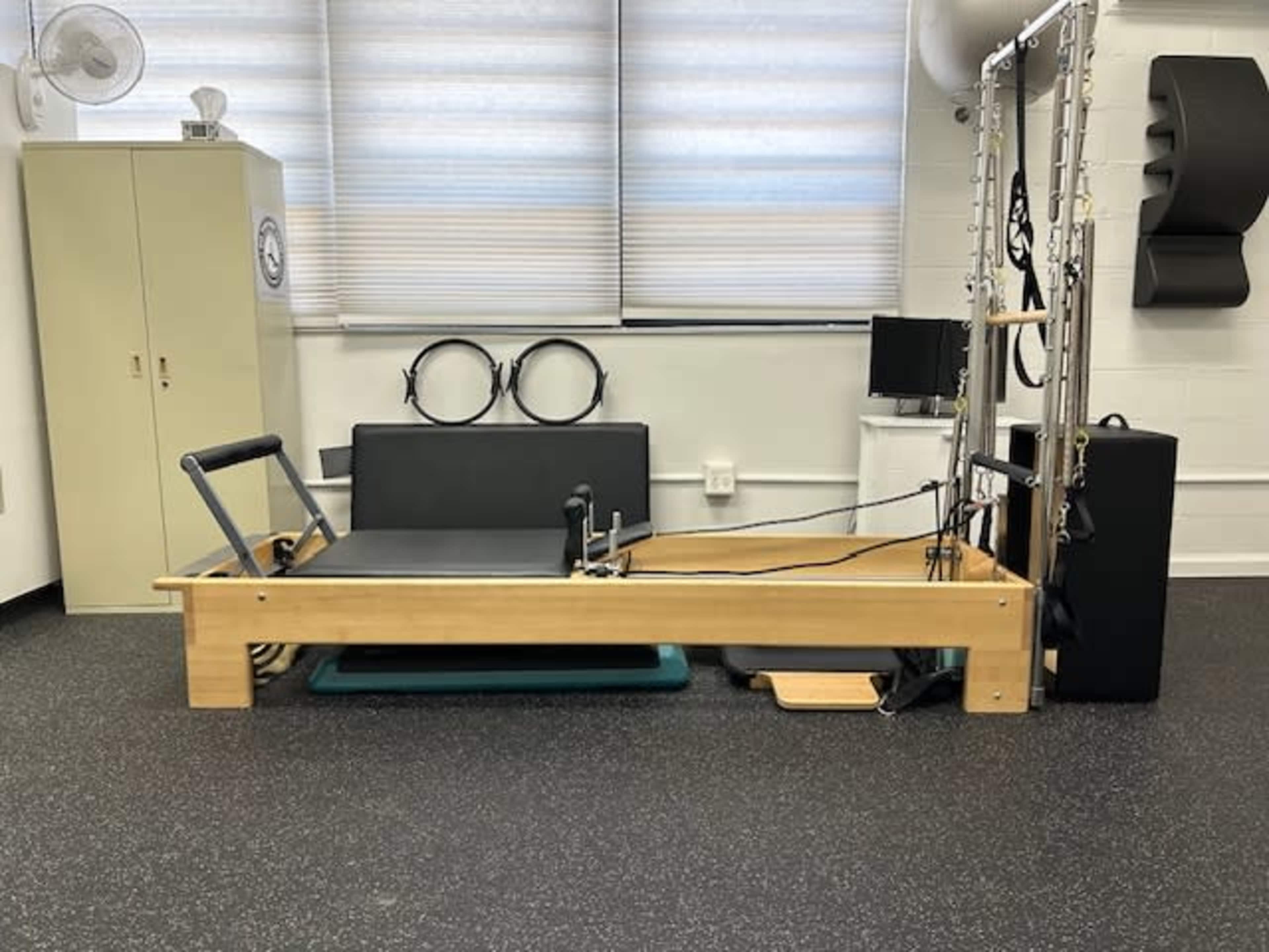 A Pilates reformer machine positioned in a studio with exercise accessories, such as rings and a television.