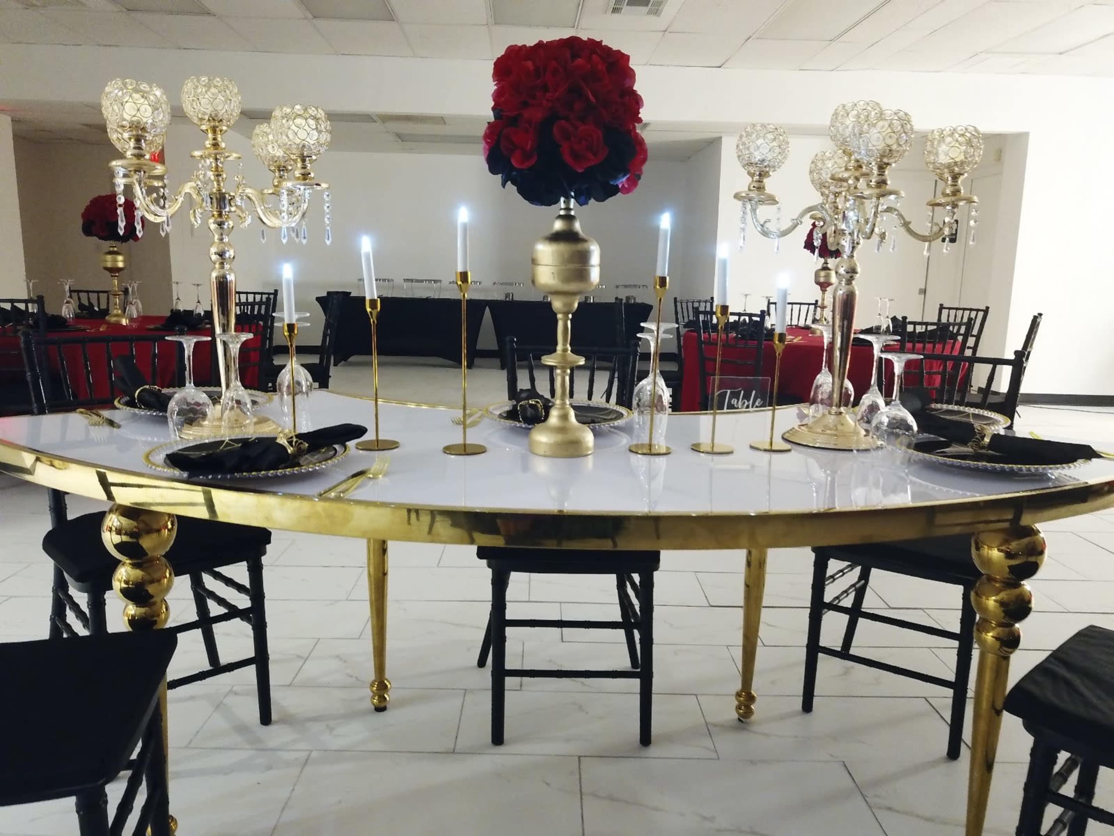 A long, elegantly set table features gold decor, candelabras, and red floral arrangements in a white and black dining room.
