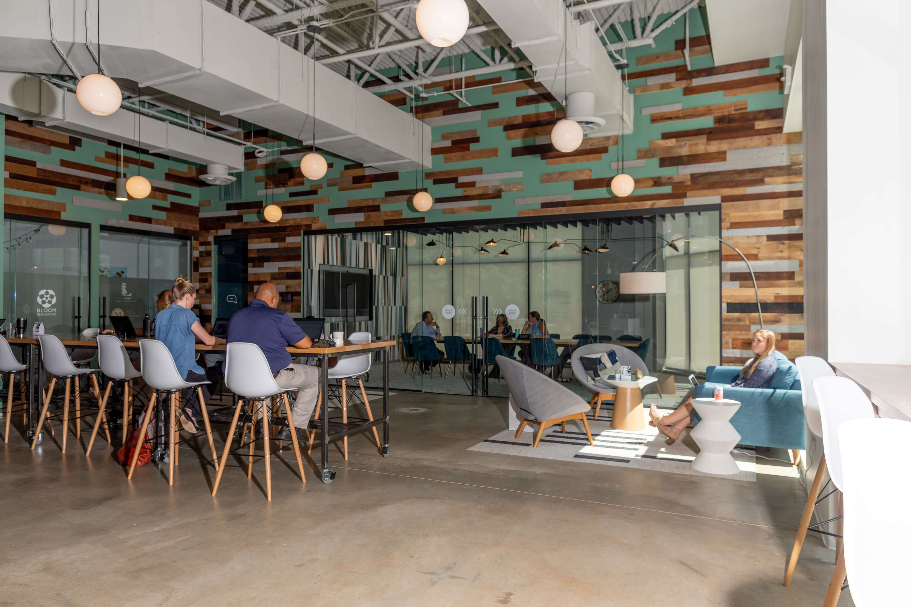 A modern office space with a mix of seating arrangements, including a bar table on one side and a lounge area on the other, against a backdrop of wooden wall panels.