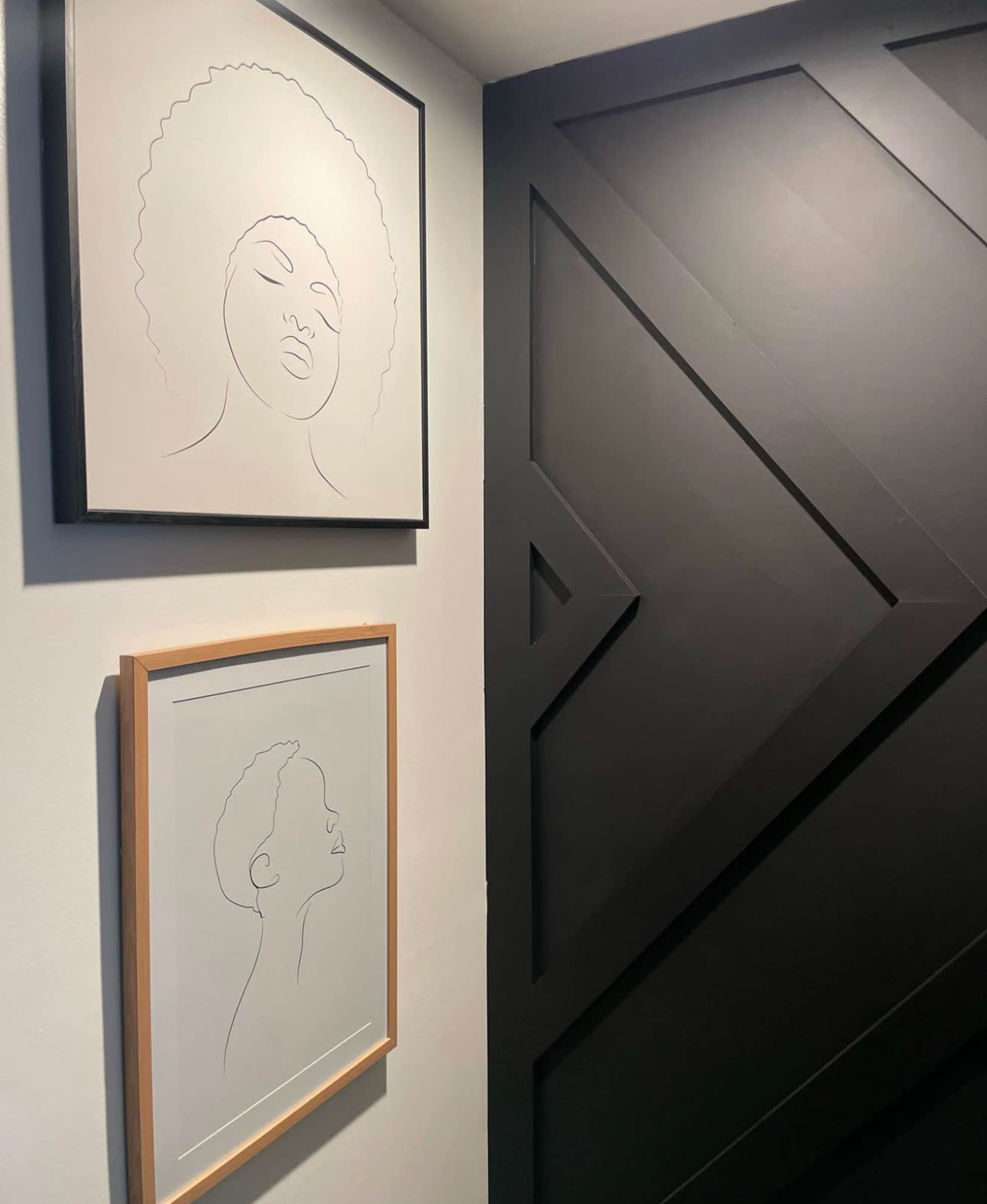 The image shows two line drawings of human faces framed and displayed on a wall next to a geometric black panel.