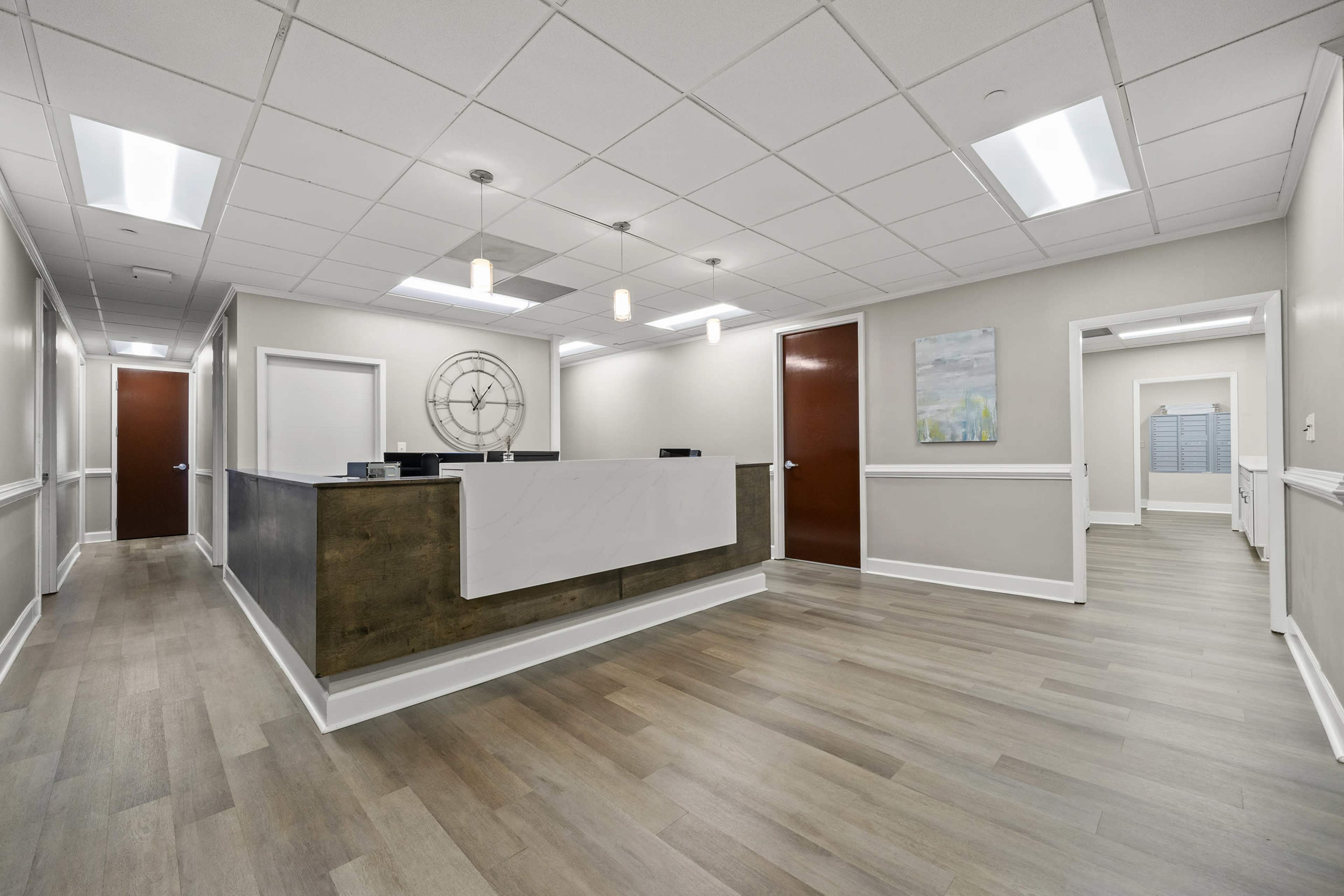 The image shows a modern office reception area with a front desk and hallway leading to additional rooms.