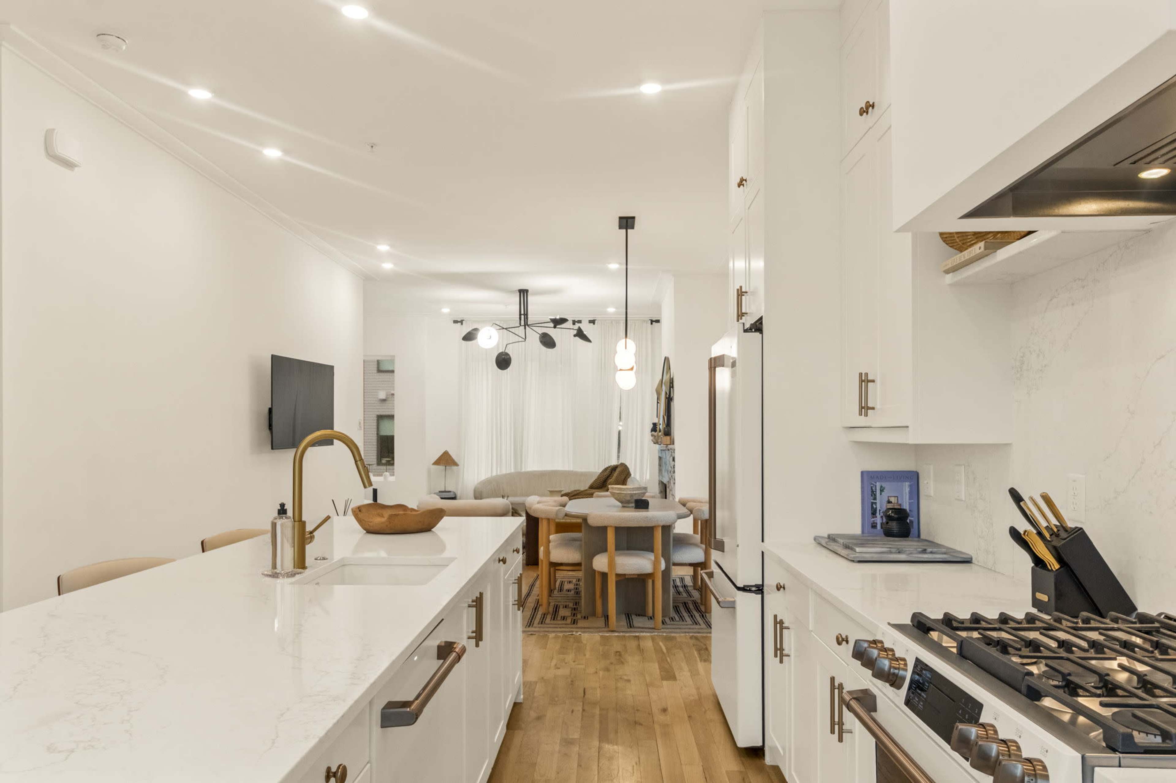 The image shows a modern kitchen with a large island, stainless steel appliances, and a dining area in an adjacent space featuring a table and chairs.