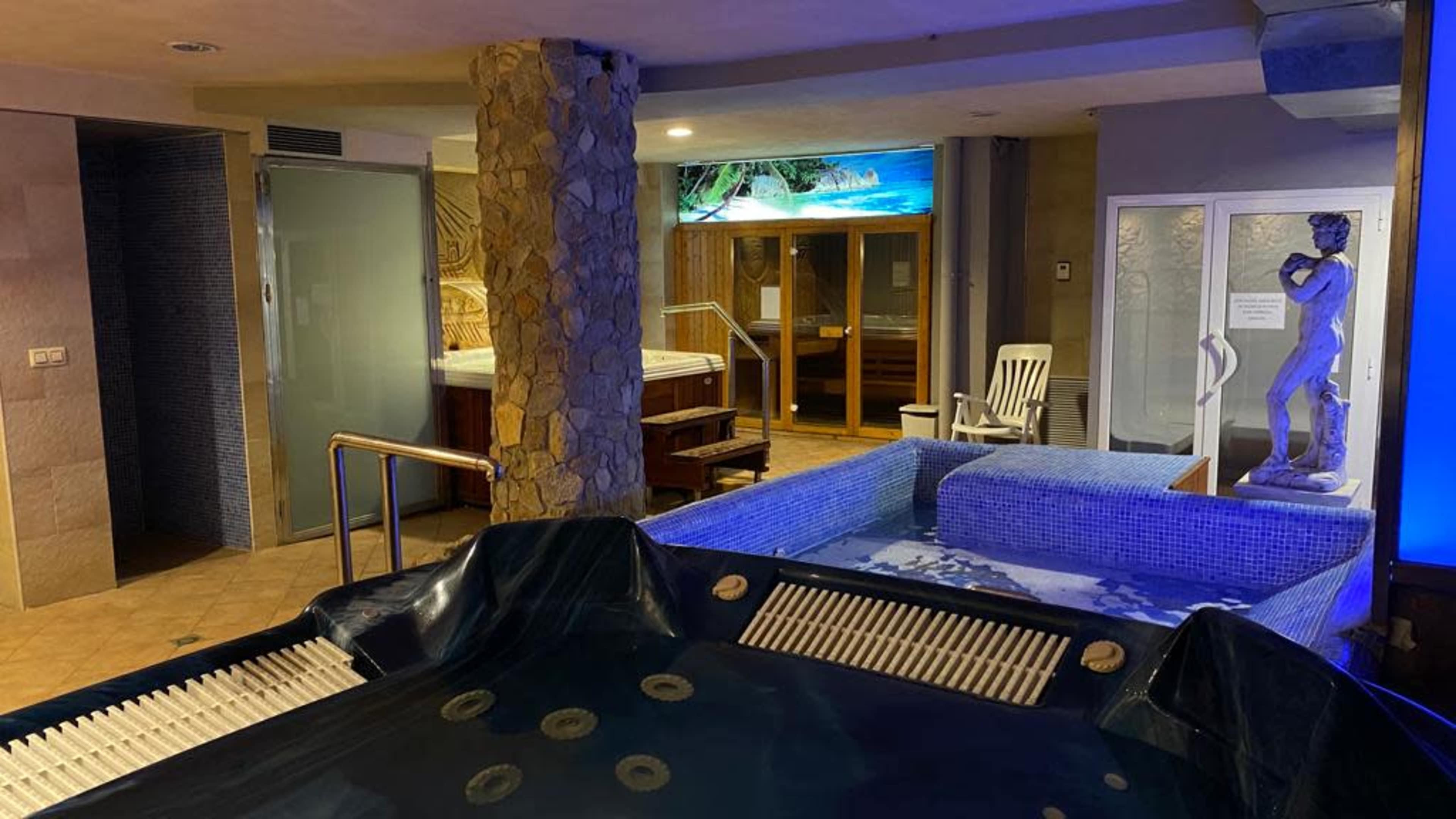 An indoor spa area featuring a hot tub, a sauna, and a decorative statue.
