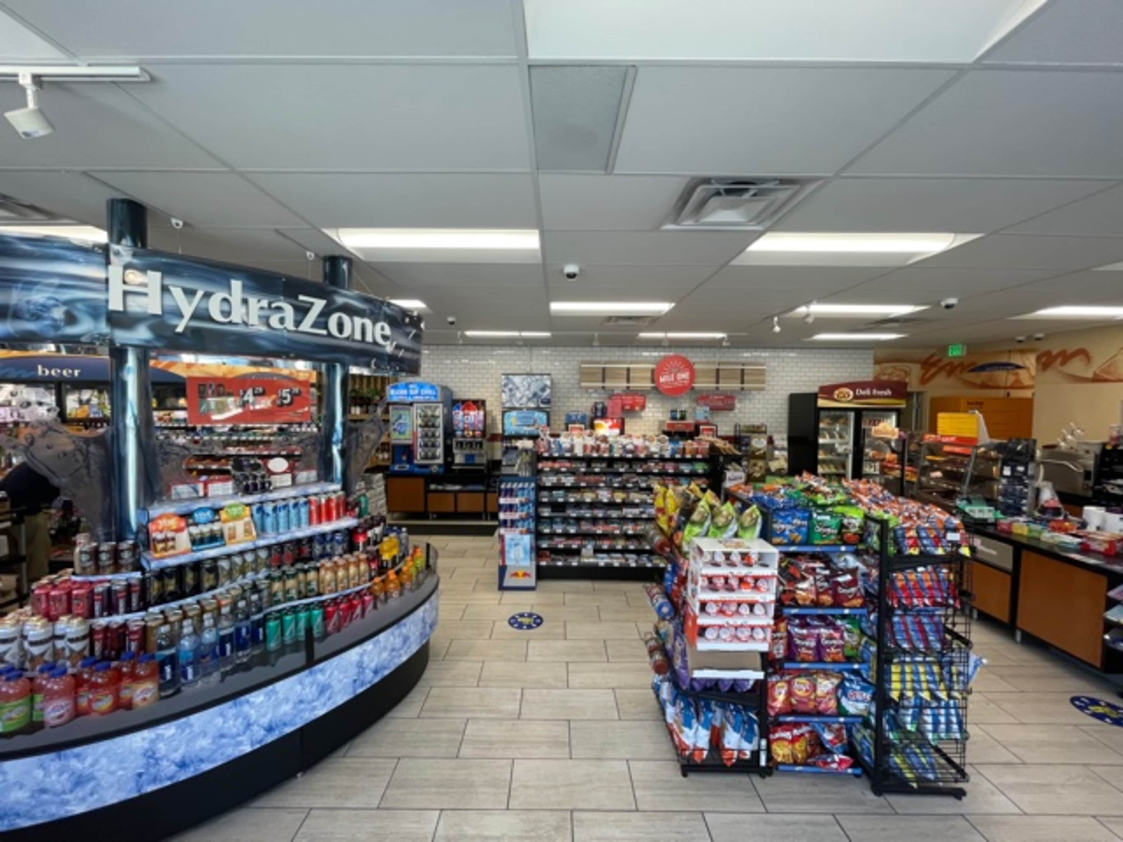 The image shows the interior of a convenience store with various beverage and snack displays, featuring a section labeled "HydraZone" on the left and snack racks on the right.