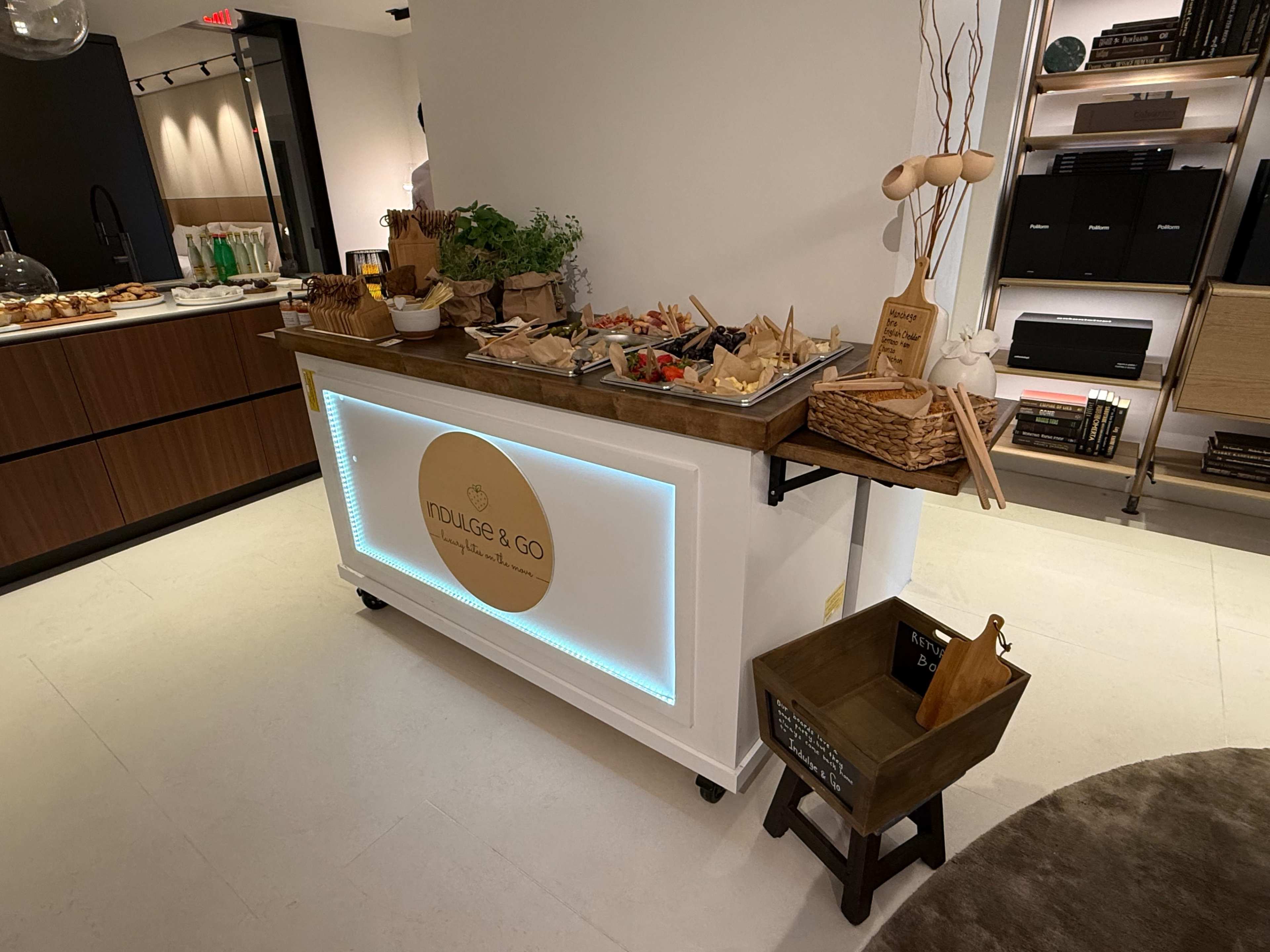 The image shows a food display counter labeled "INDULGE & GO," featuring various food items arranged on it.