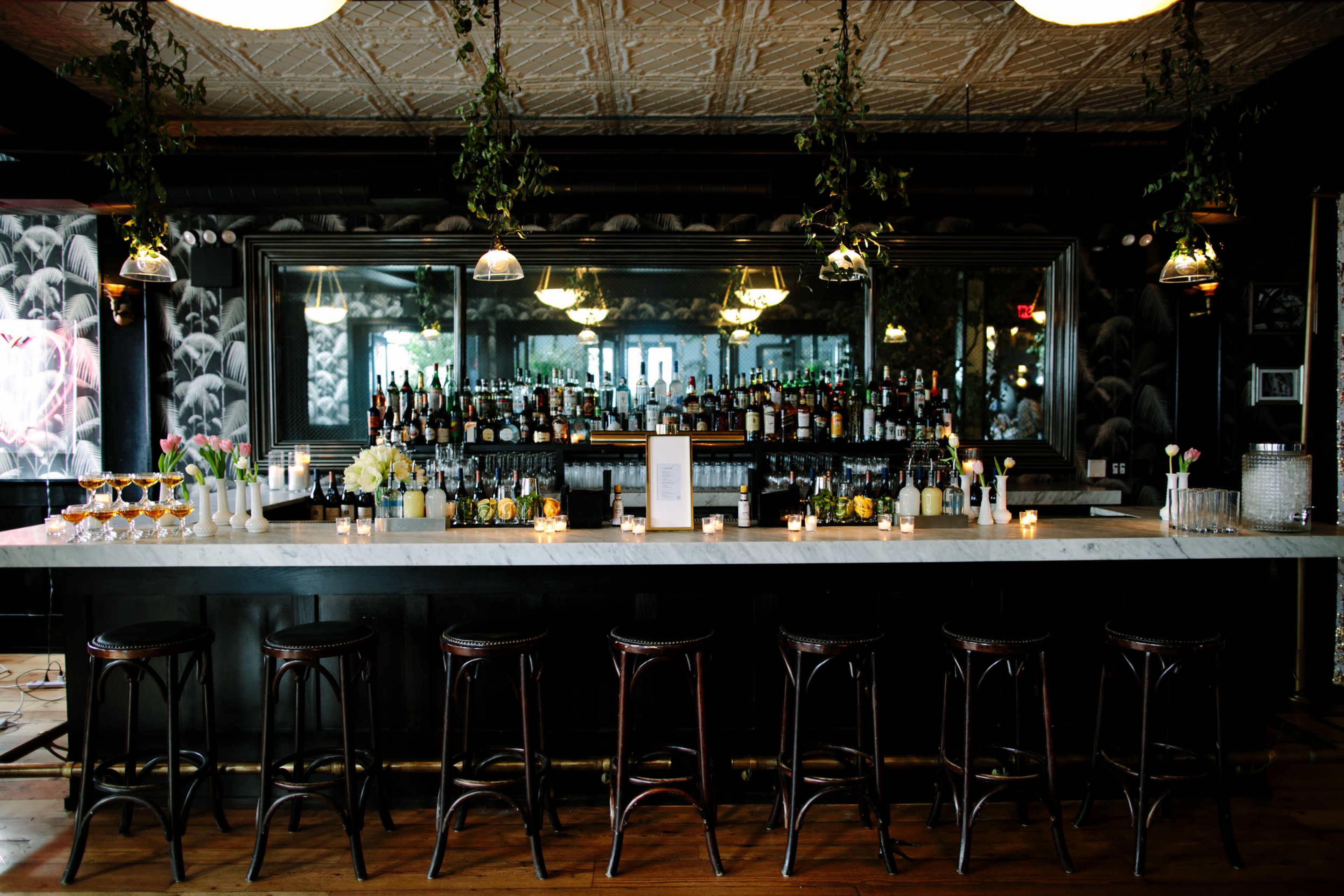 A stylish bar with a long marble countertop, several bar stools, and a large mirror reflecting shelves stocked with a variety of alcoholic beverages.