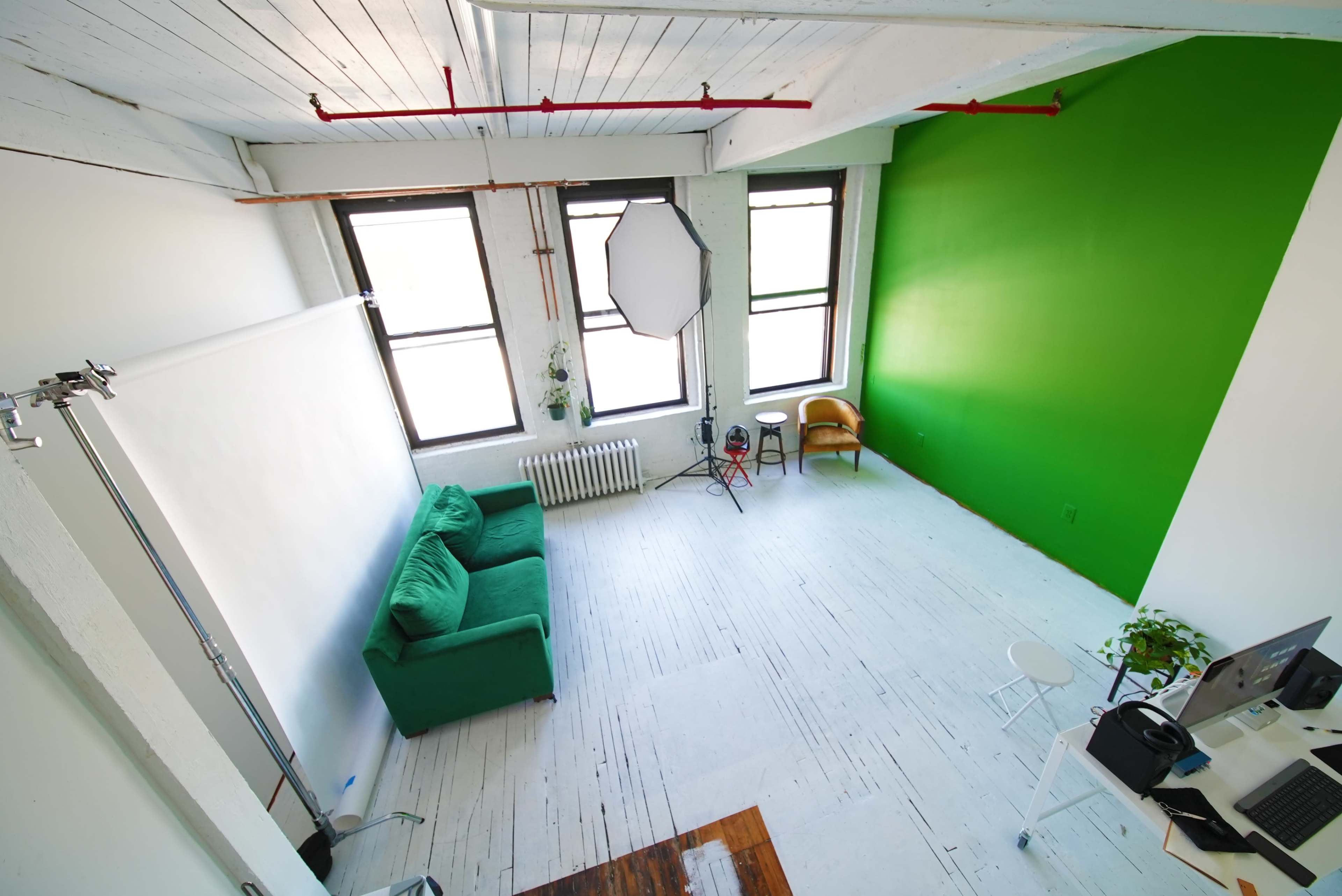 A bright, spacious studio with a green accent wall, a green sofa, a white workspace, and a light setup.
