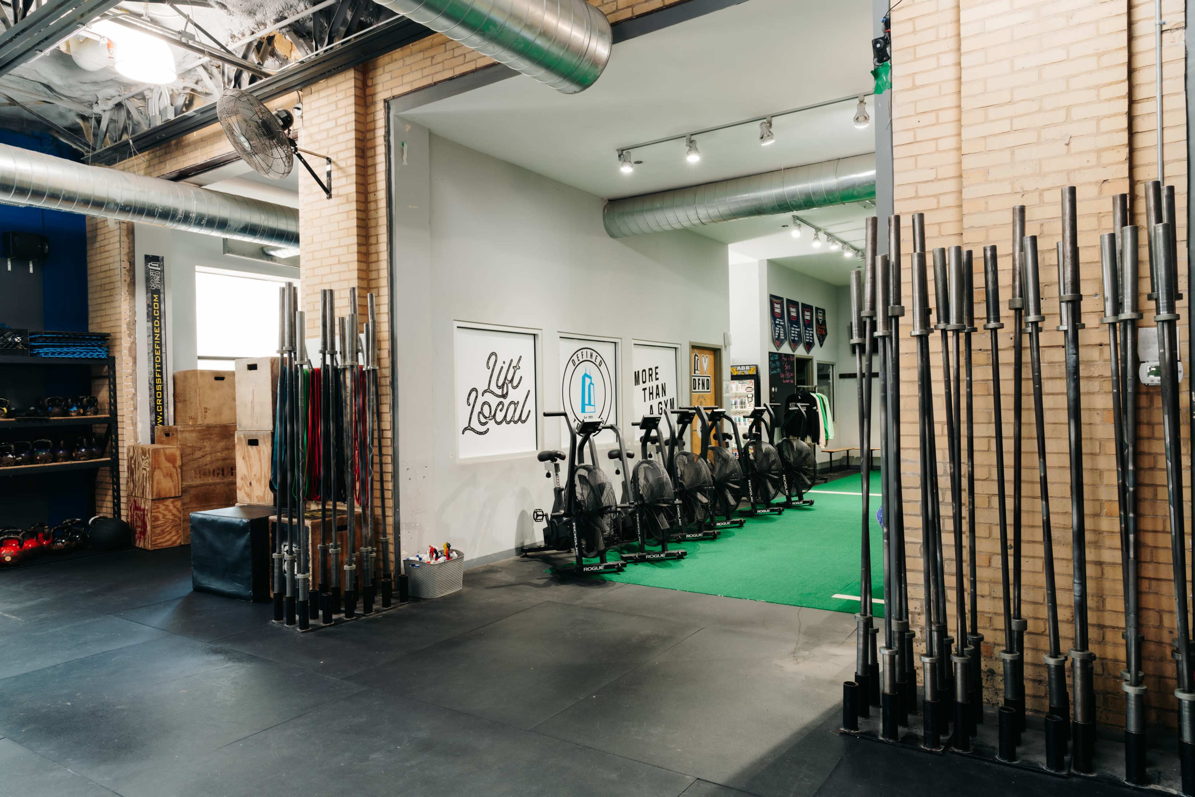 The image shows a gym interior with various weightlifting equipment aligned along the walls and a green exercise area in the back.