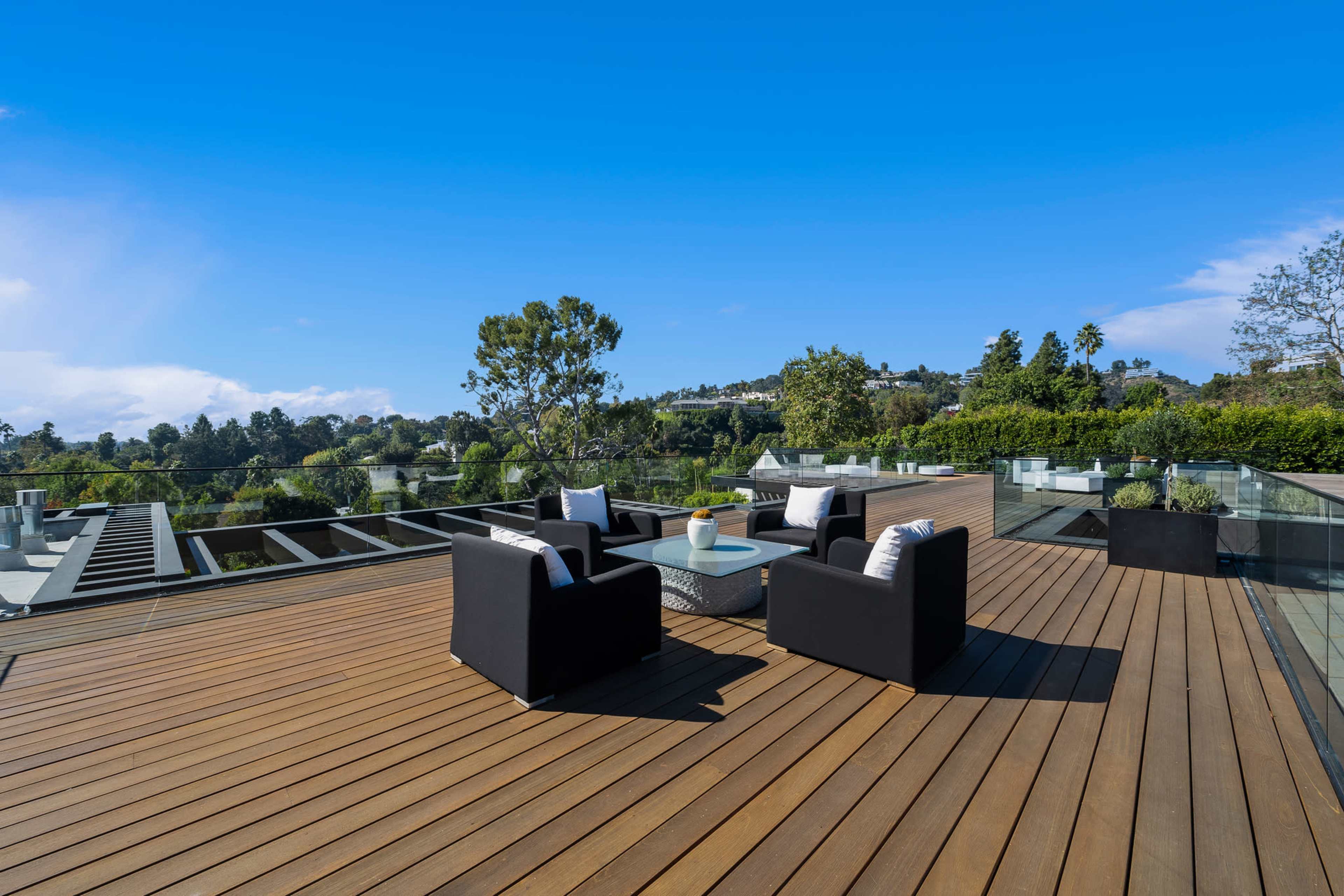 A modern rooftop terrace features black seating arrangements and a glass railing, overlooking a scenic landscape.