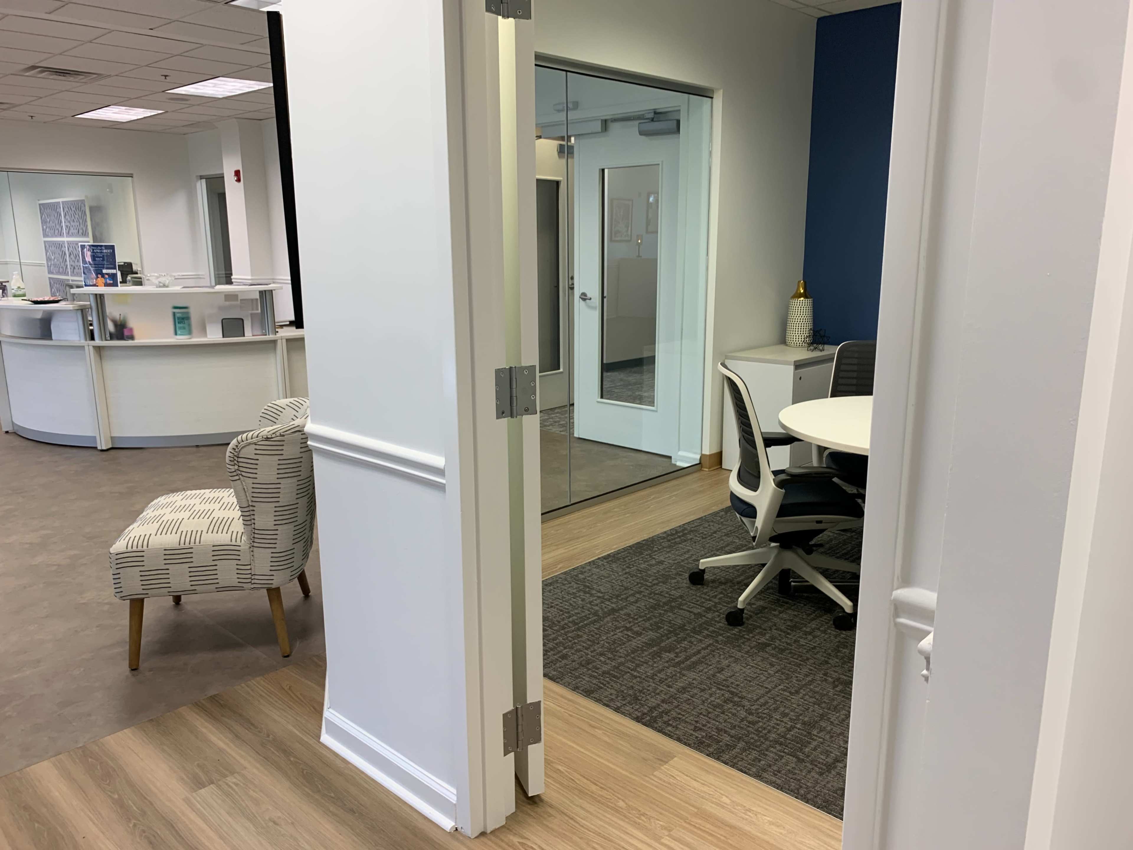 An office space features a chair near a doorway looking into a meeting room with a round table and chairs.