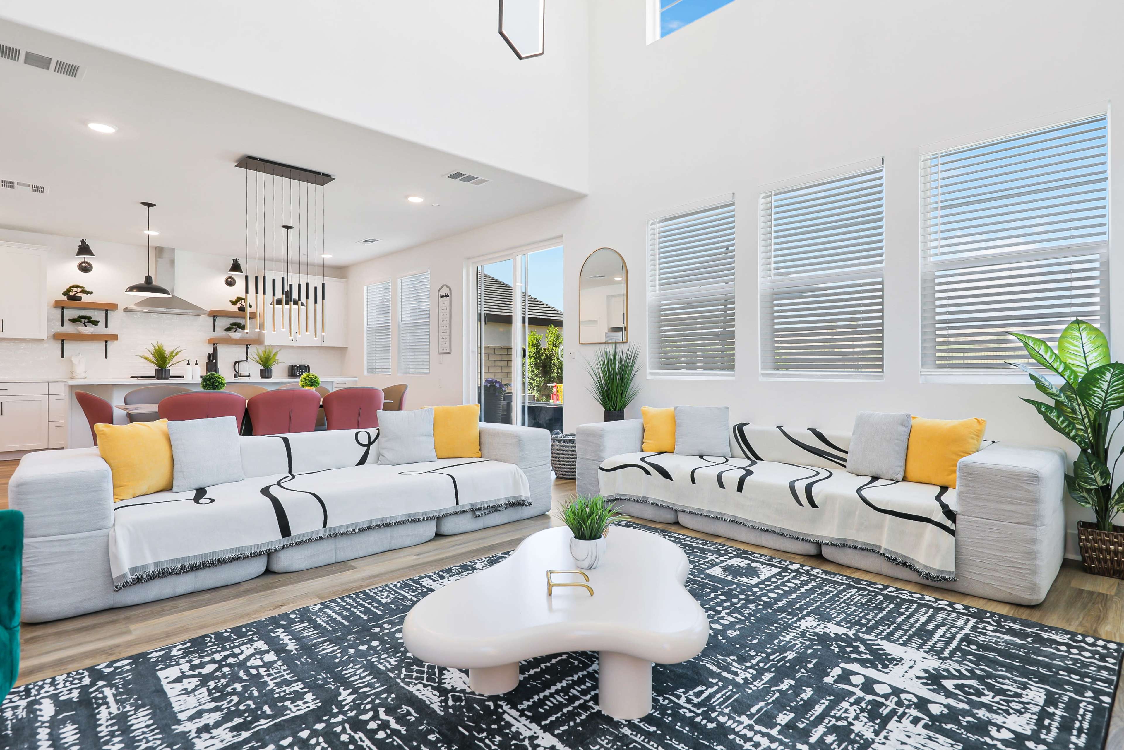 The image shows a modern living room with two couches facing each other, a round coffee table, and large windows letting in natural light.
