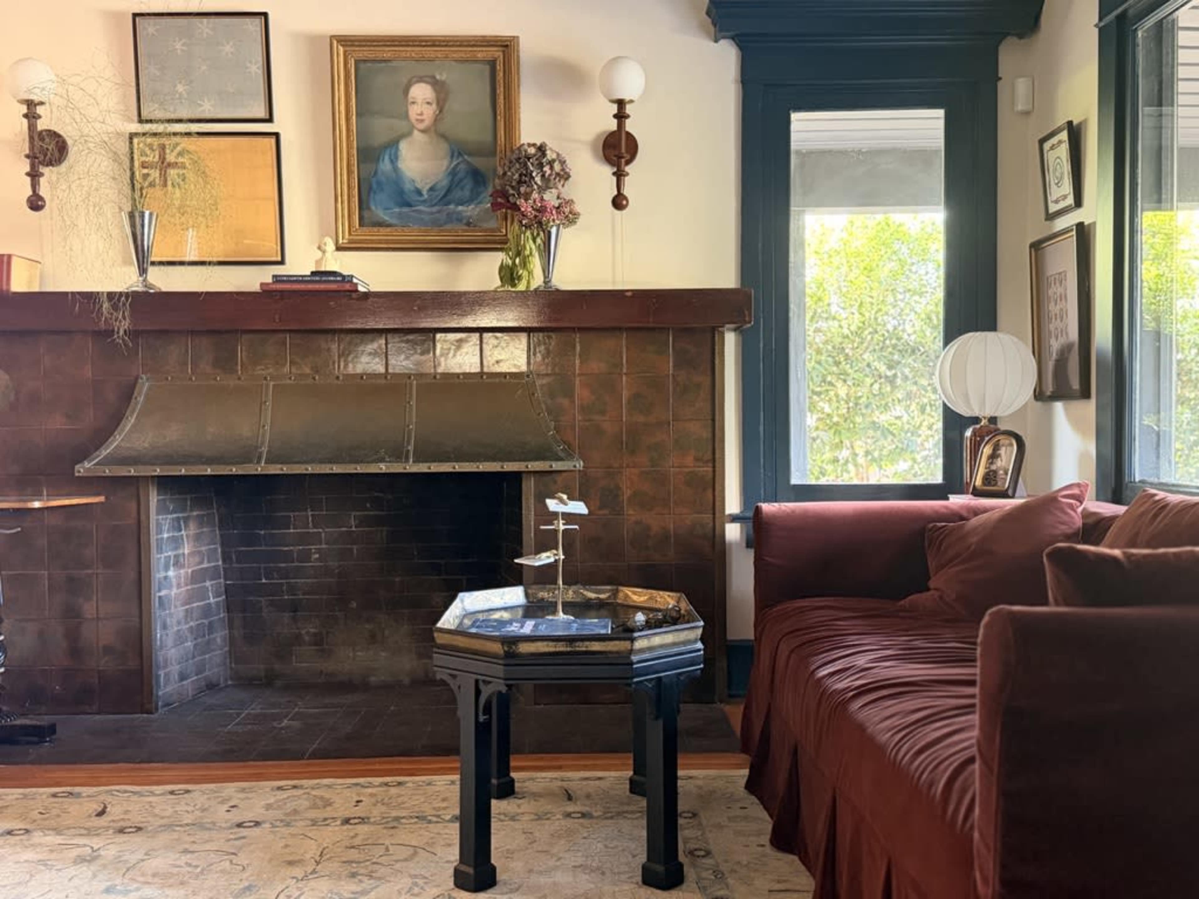 The image features a cozy living room with a red couch, a decorative fireplace with a bronze hood, and artwork hanging on the walls.