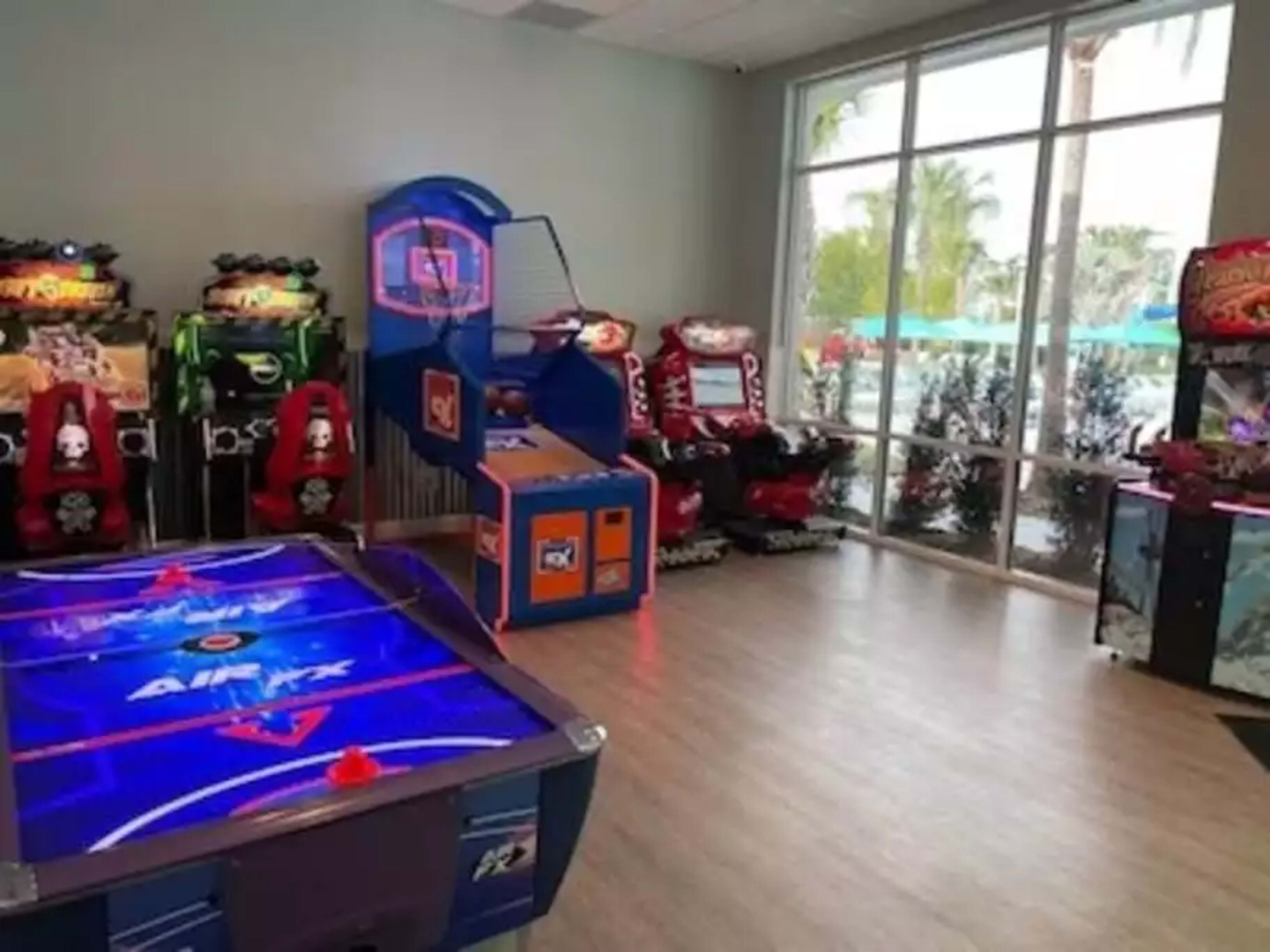 The image shows an arcade room with various gaming machines, including air hockey and basketball games, illuminated by bright lights.