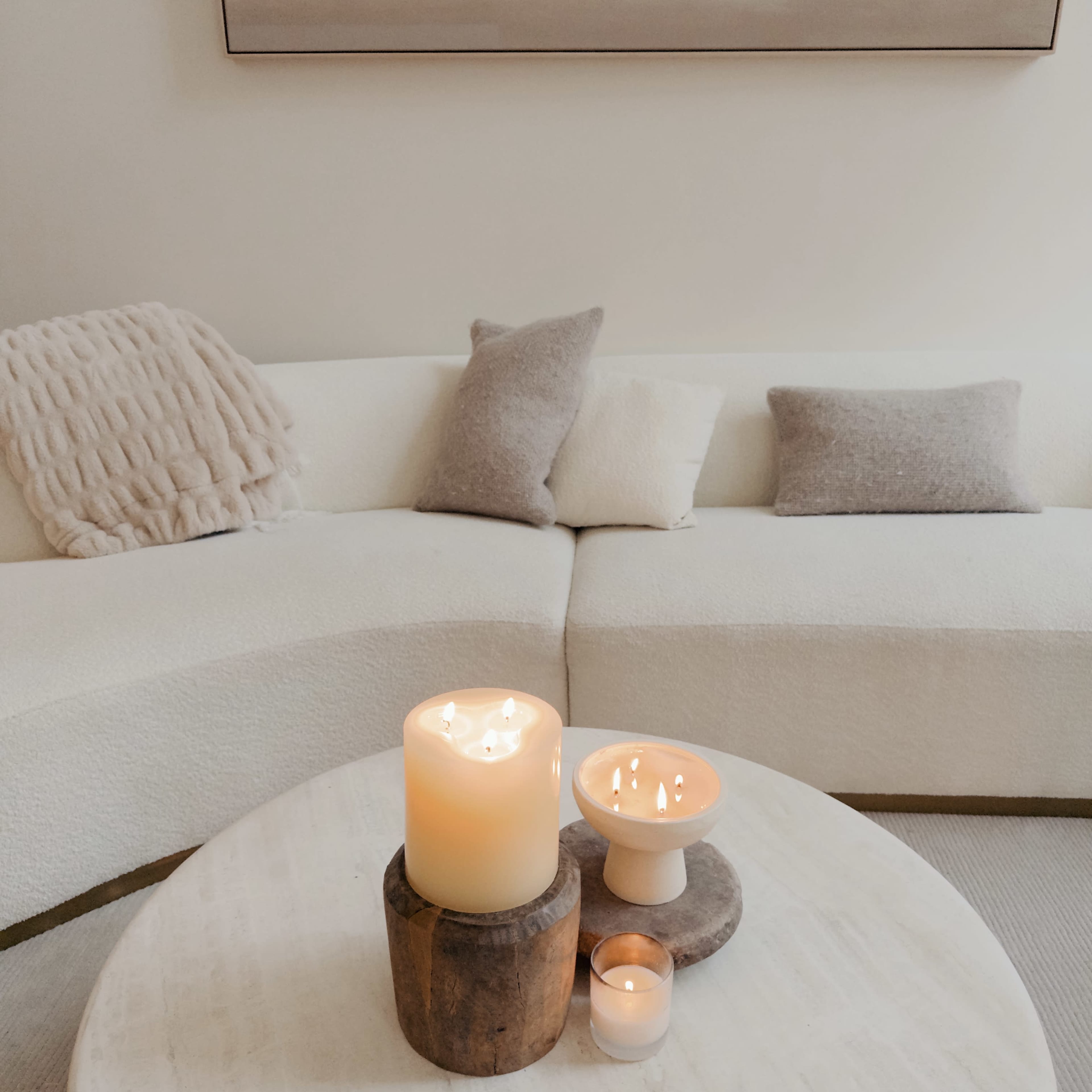 A cozy living room scene features a circular white sofa with textured throw pillows and a coffee table adorned with lit candles.