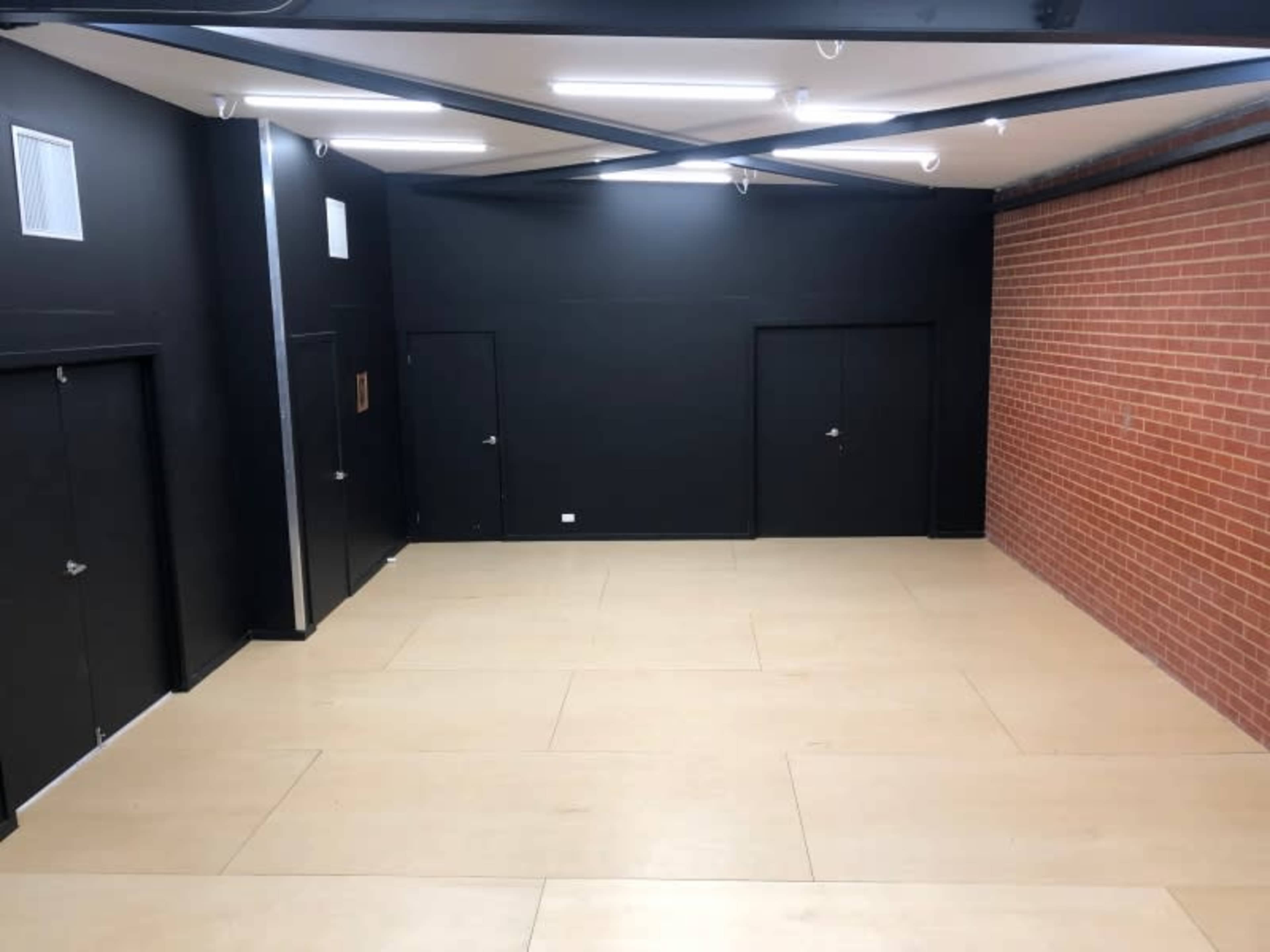 A spacious interior with black walls and two dark doors, alongside a section of exposed red brick wall, illuminated by overhead lights.