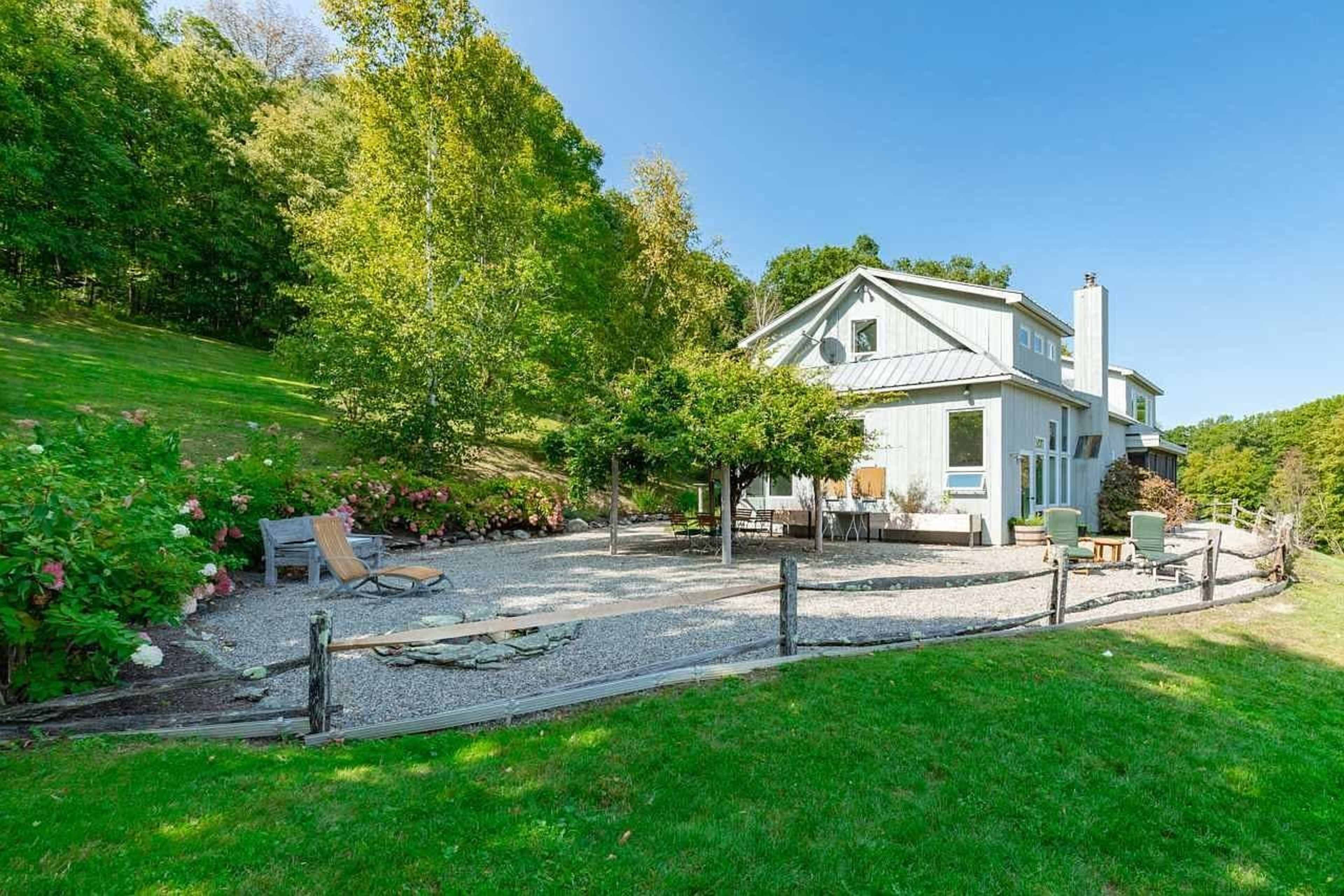 A modern house with a landscaped garden and gravel patio is set against a backdrop of trees.