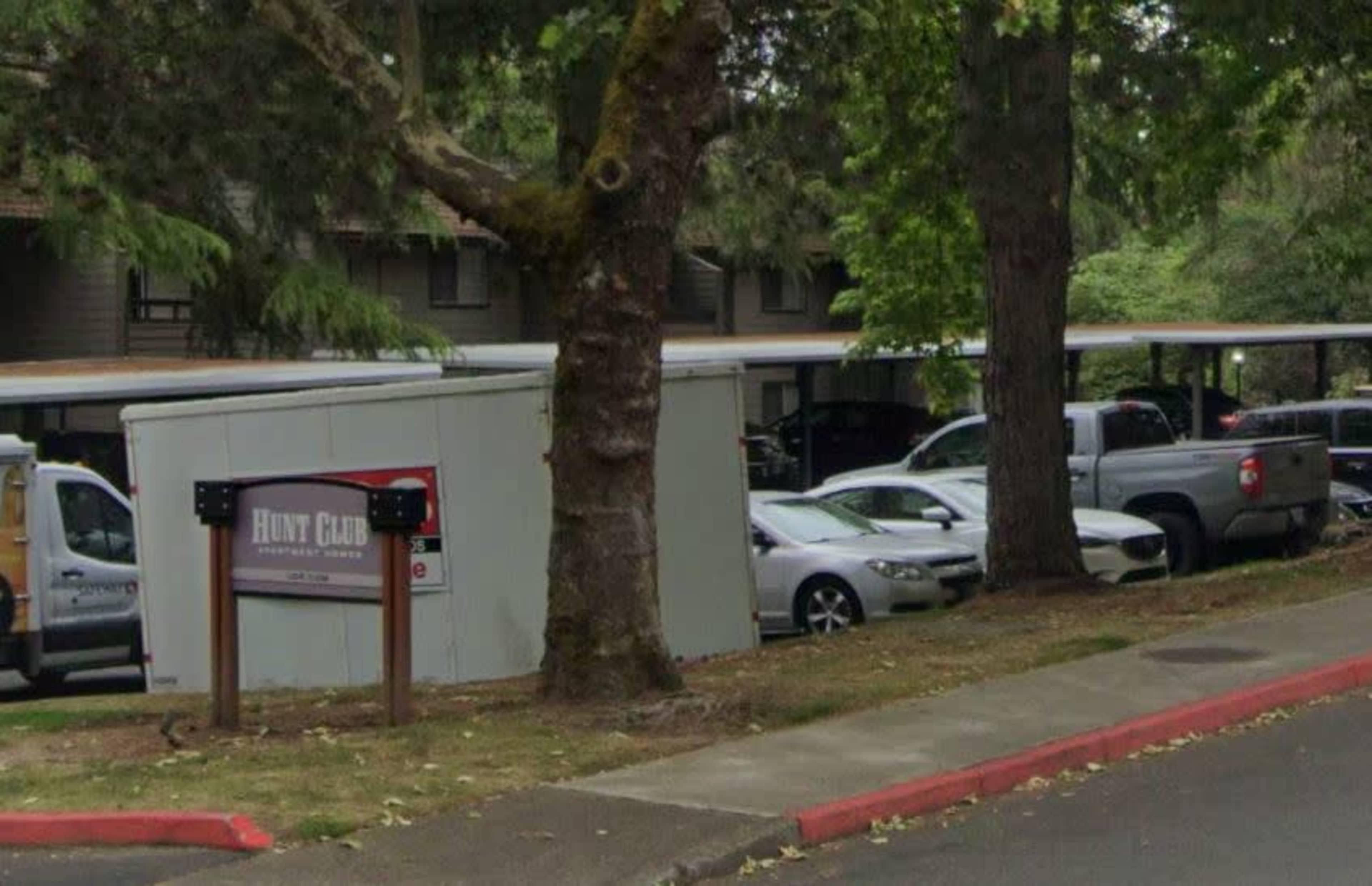 A parking area behind a sign for "Hunt Club" near several cars and trees.