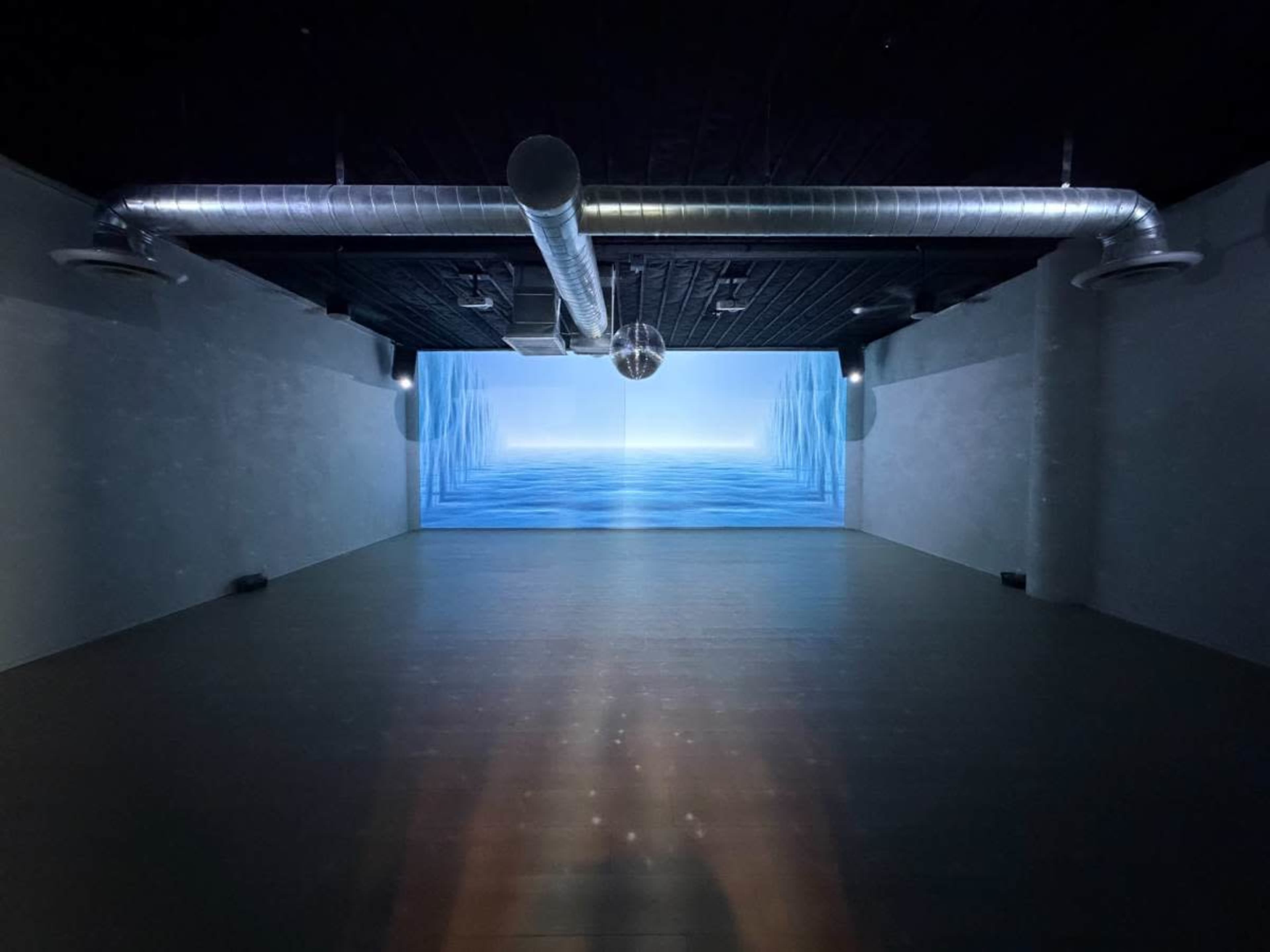 The image shows a large, empty room with a curved wall displaying a blue ocean scene and suspended overhead ductwork.