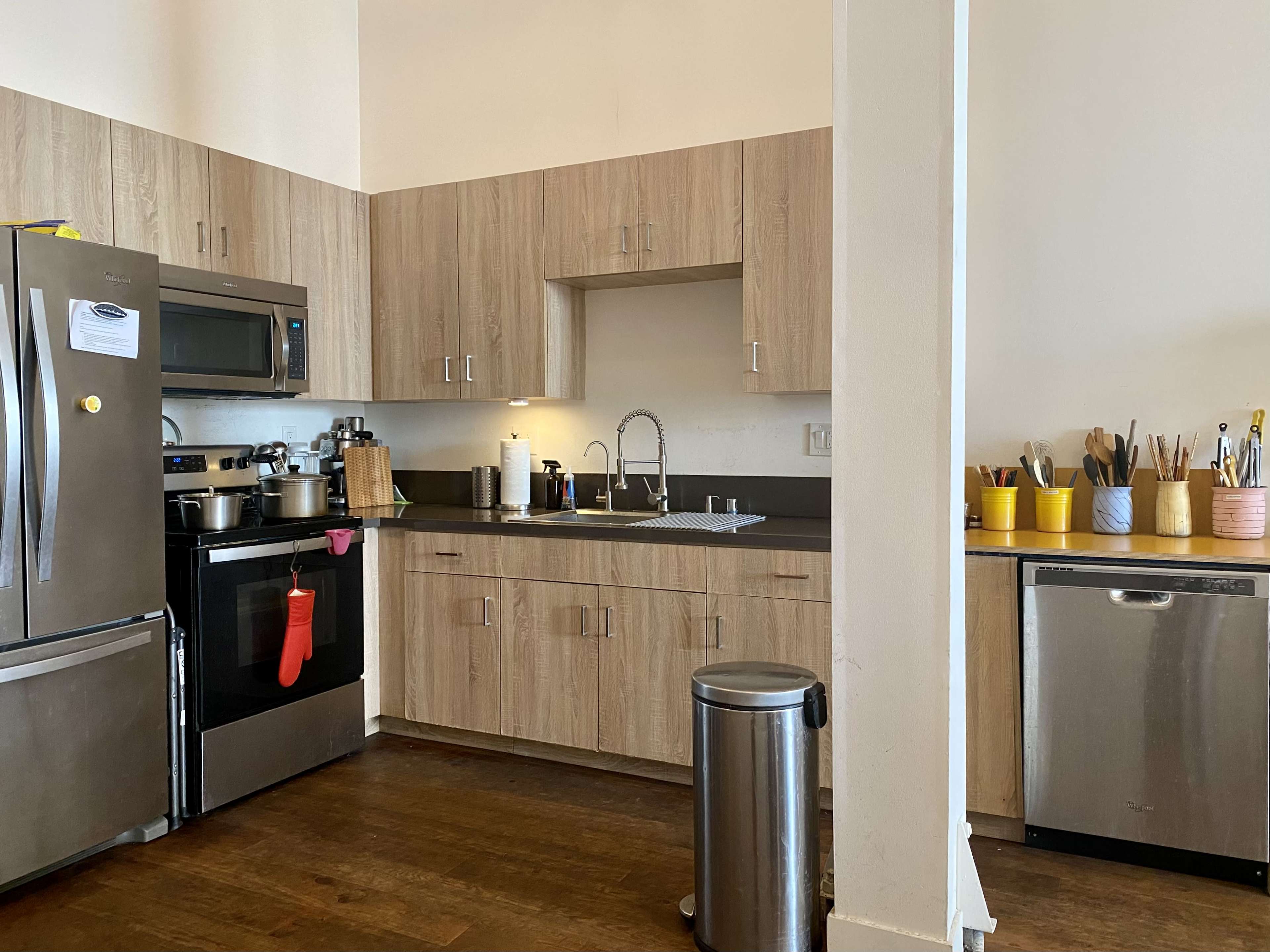 A modern kitchen features stainless steel appliances, wooden cabinets, and a sink with various utensils displayed in colorful containers.