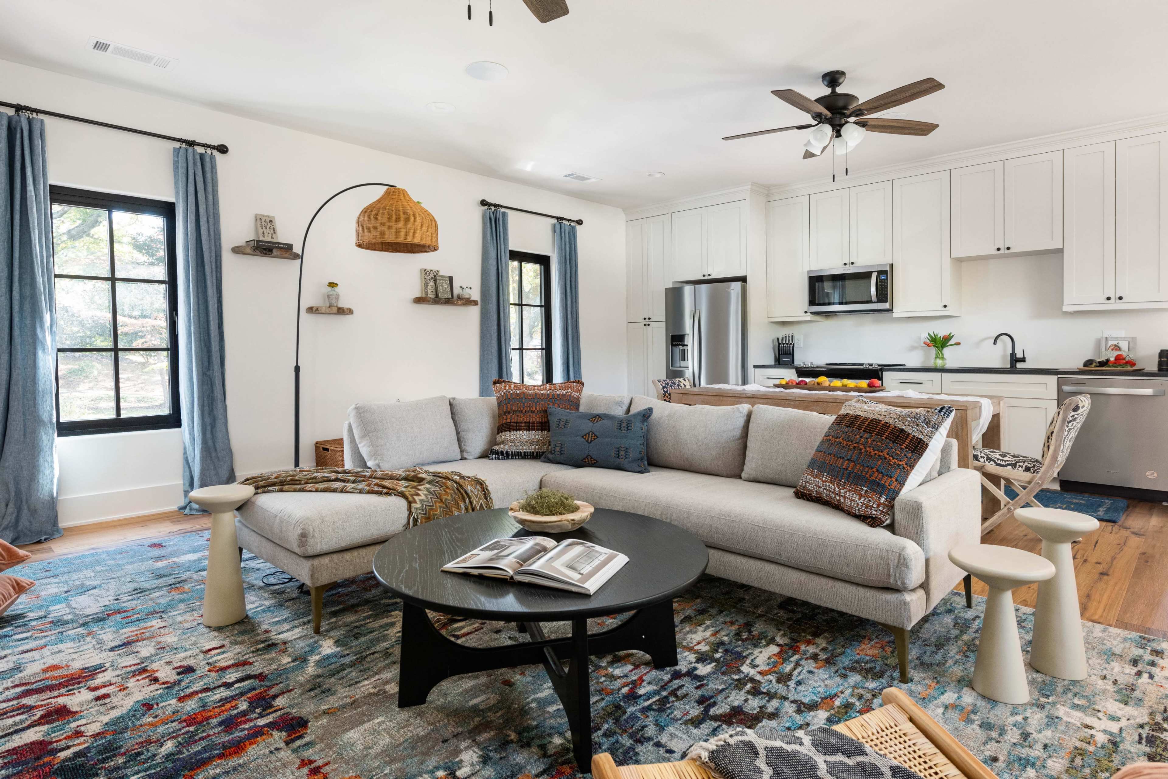 A modern living room features a light gray sectional sofa, a black coffee table, and a kitchen area in the background.