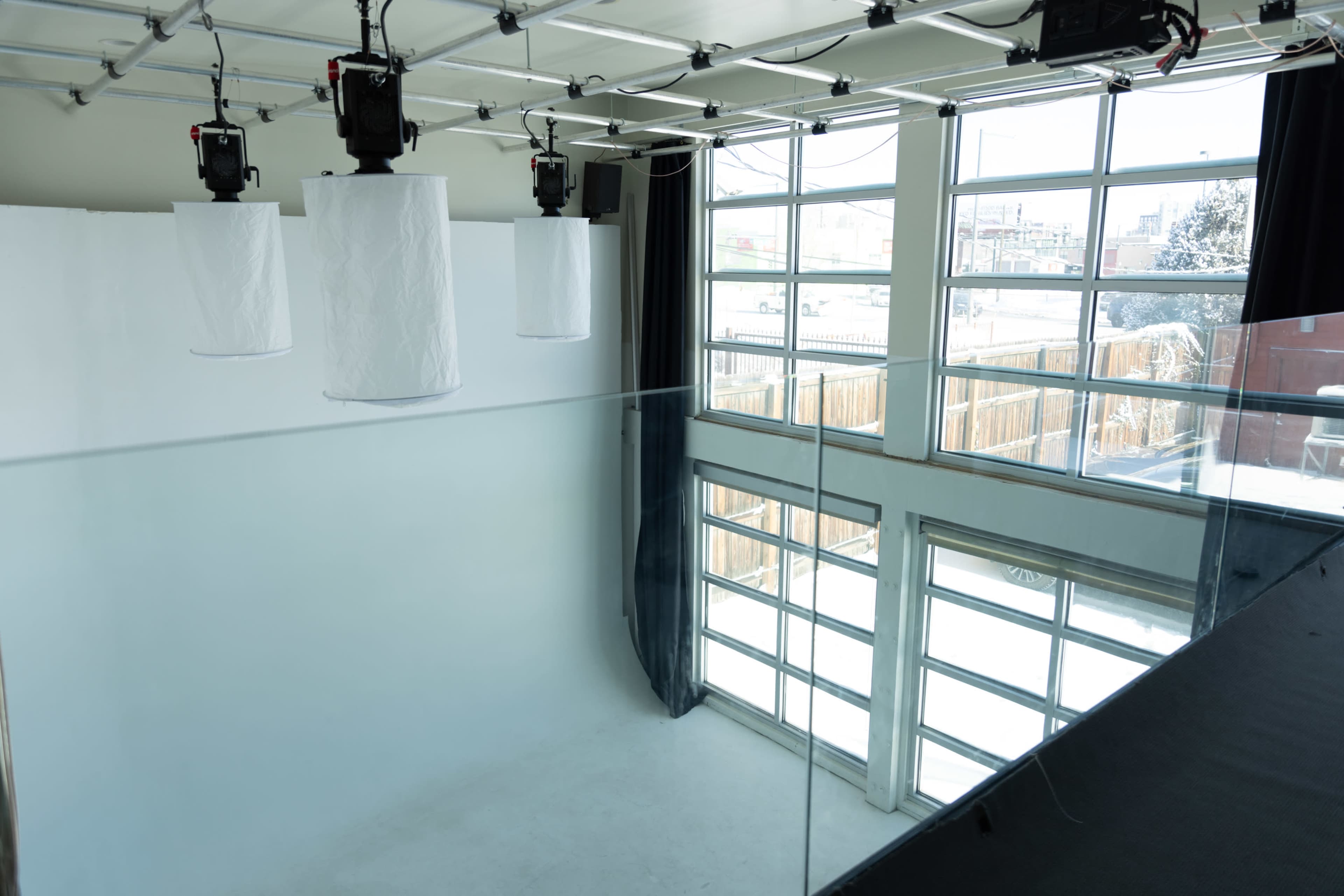 A spacious photography studio with large windows, white backdrop, and overhead lighting fixtures.
