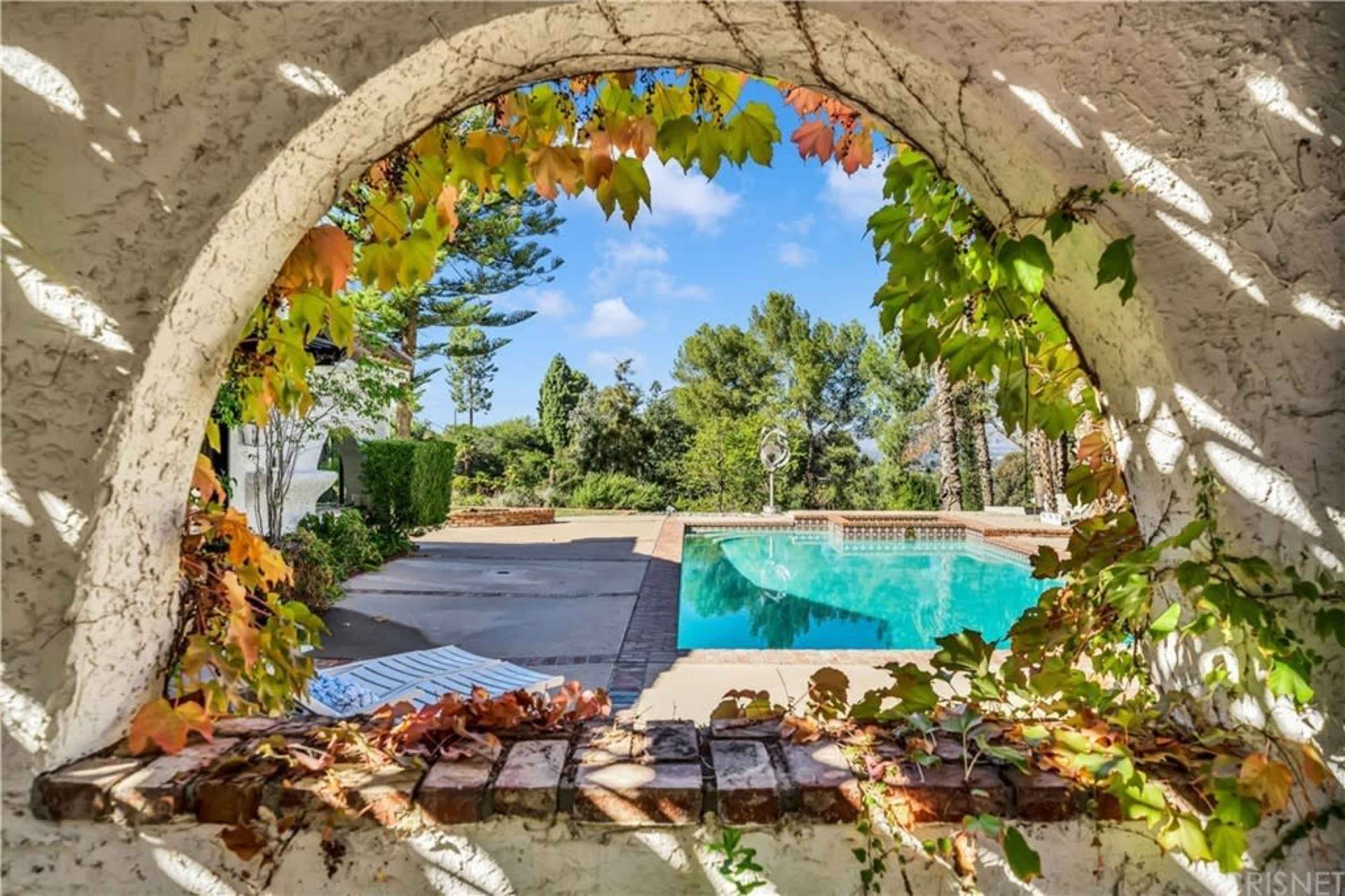 A circular stone arch framing a view of a swimming pool surrounded by greenery.