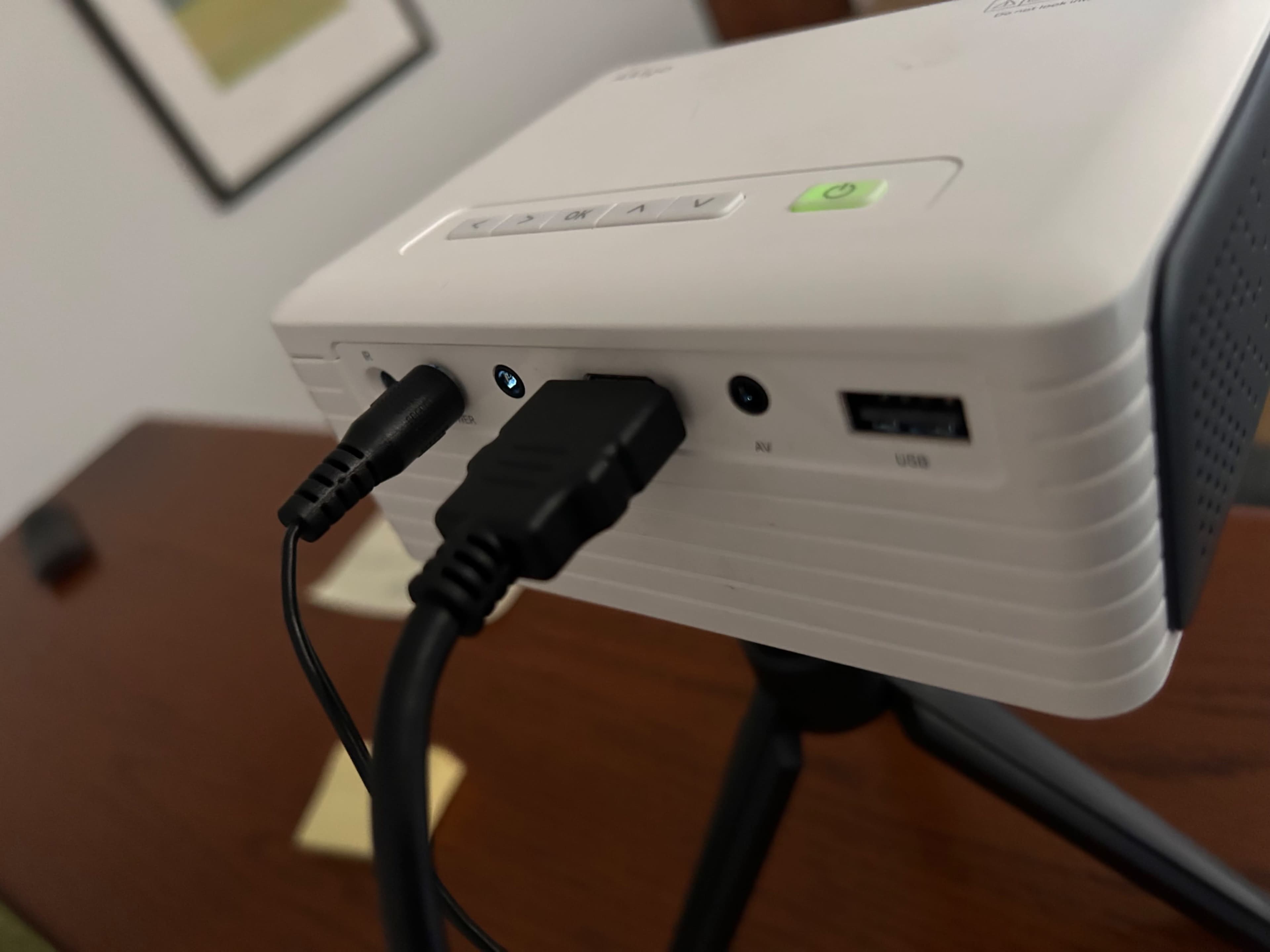 A compact projector is connected with audio and USB cables on a wooden table.