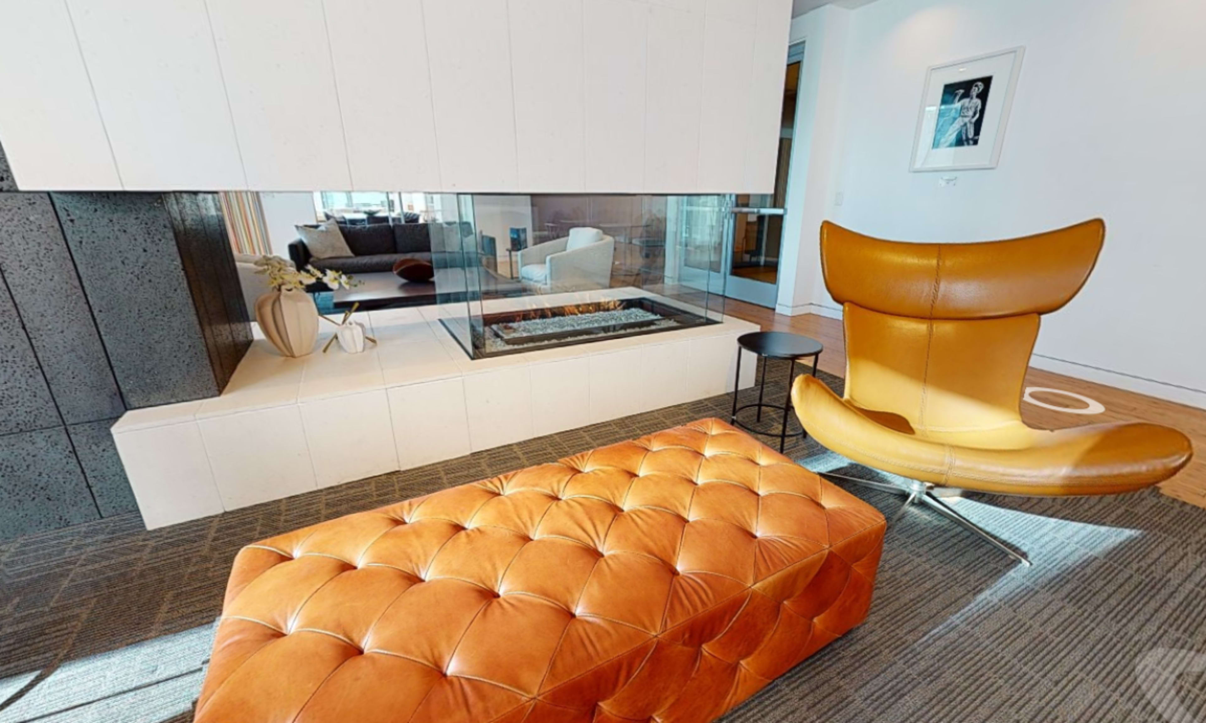 A modern living space featuring a tufted orange lounge chair and ottoman near a sleek fireplace with a glass front.