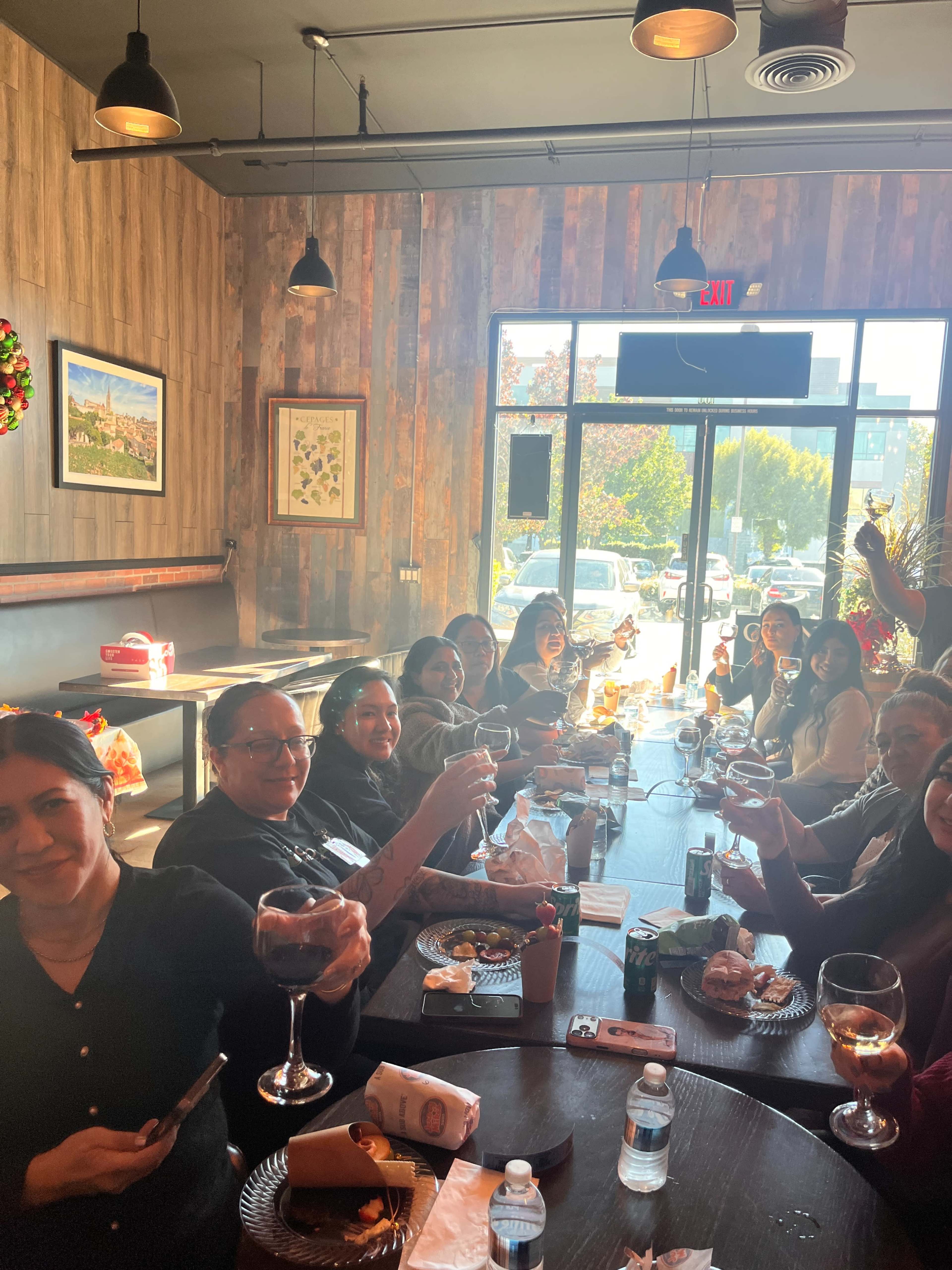 A group of people sit at a long table inside a restaurant, raising glasses in a toast while enjoying food and drinks.