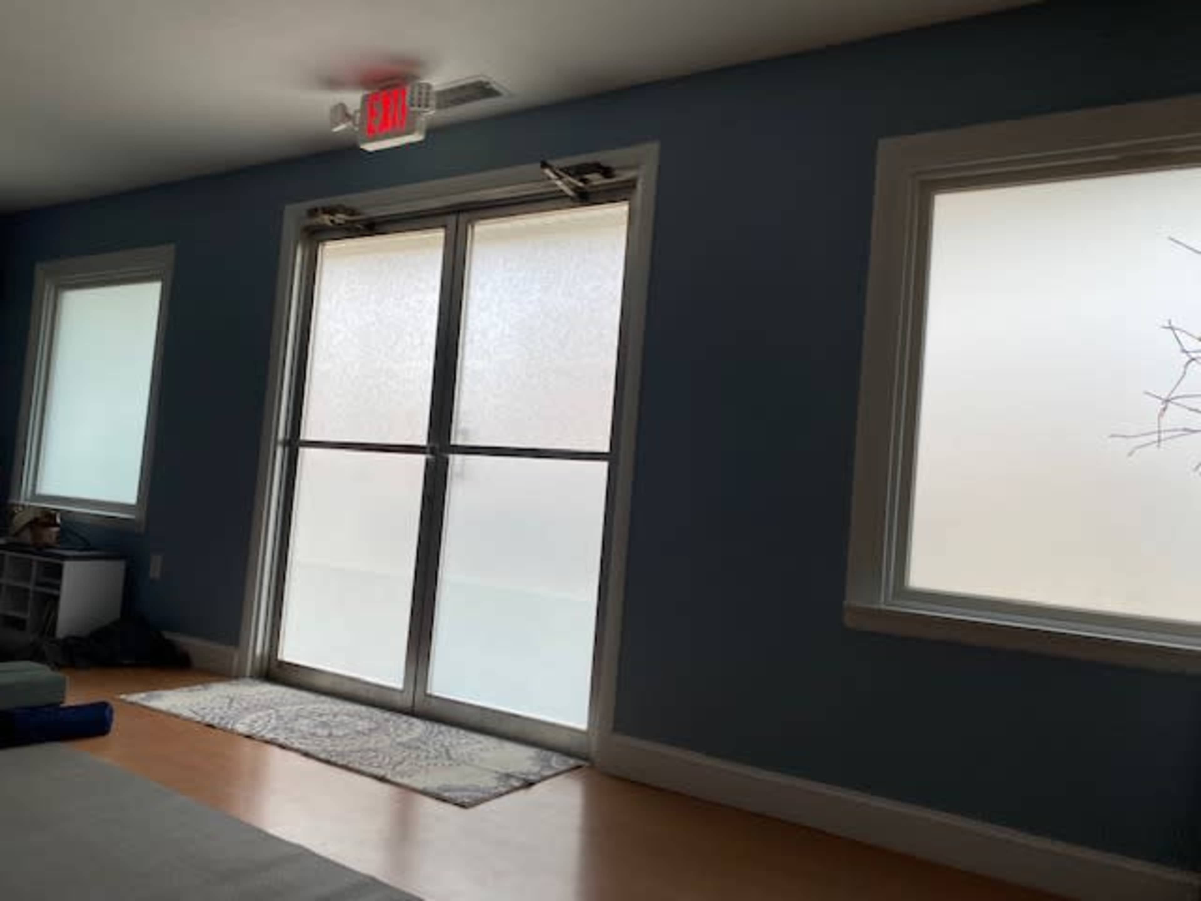 A room with large frosted glass doors and two frosted windows on a light blue wall, along with a small rug and a shelf in the corner.