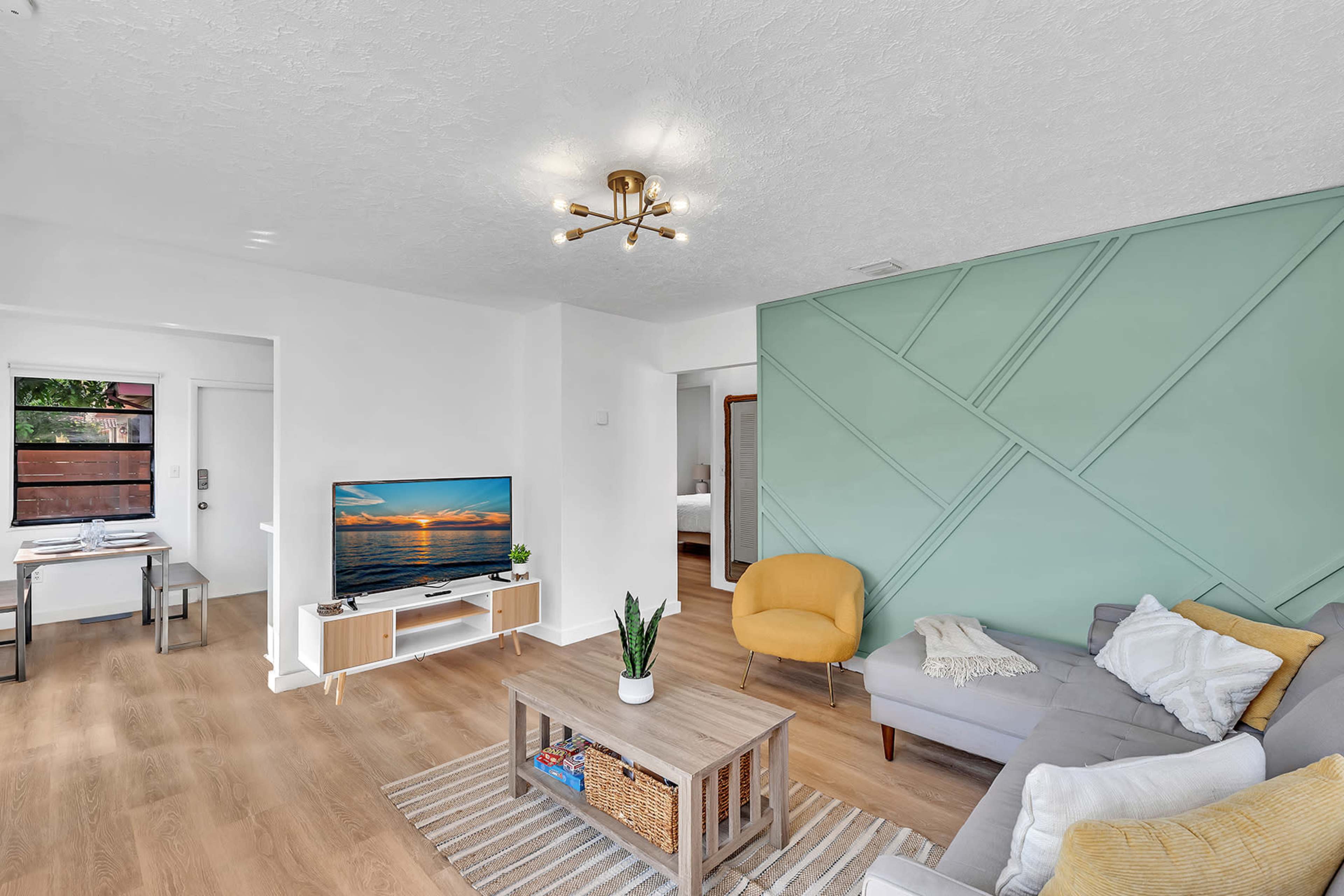 The living room features a gray sectional sofa, a wooden coffee table, and a television against a wall with a geometric green accent.