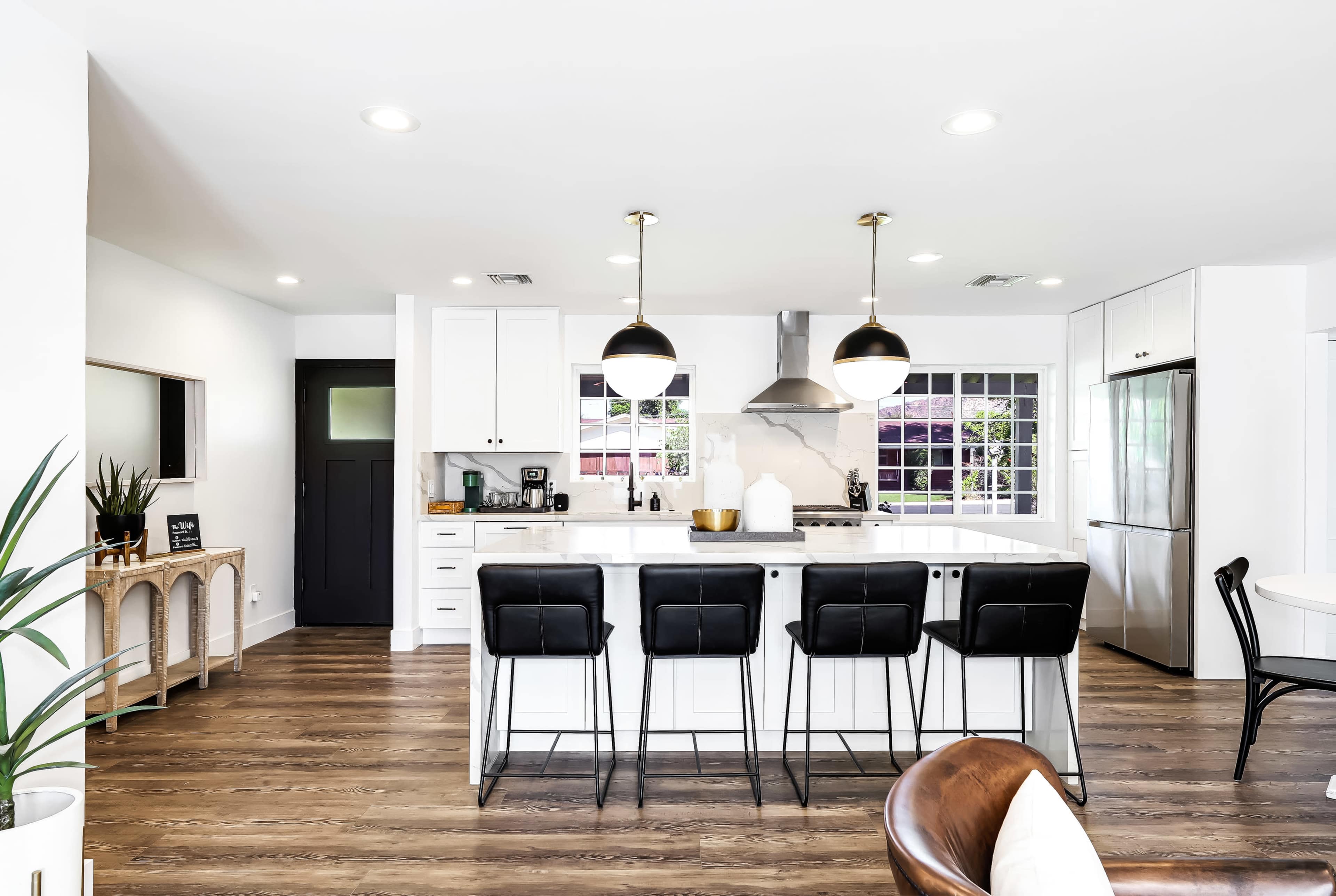 A modern kitchen features a large island with seating, black pendant lights, and stainless steel appliances.